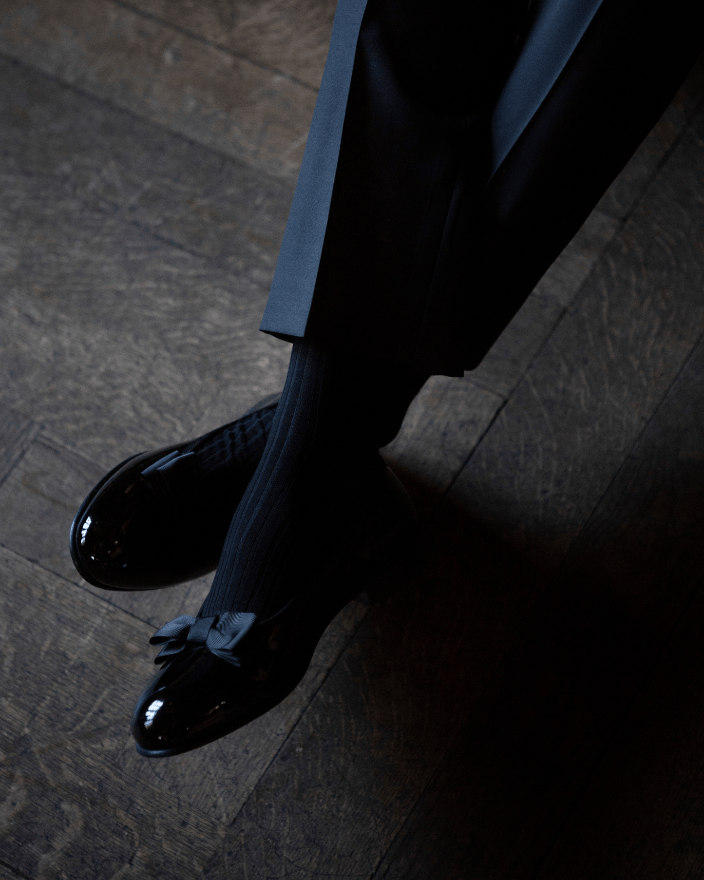 Close-up on a person wearing Rosendal – Black Patent Leather opera pumps with black trousers and ribbed socks.