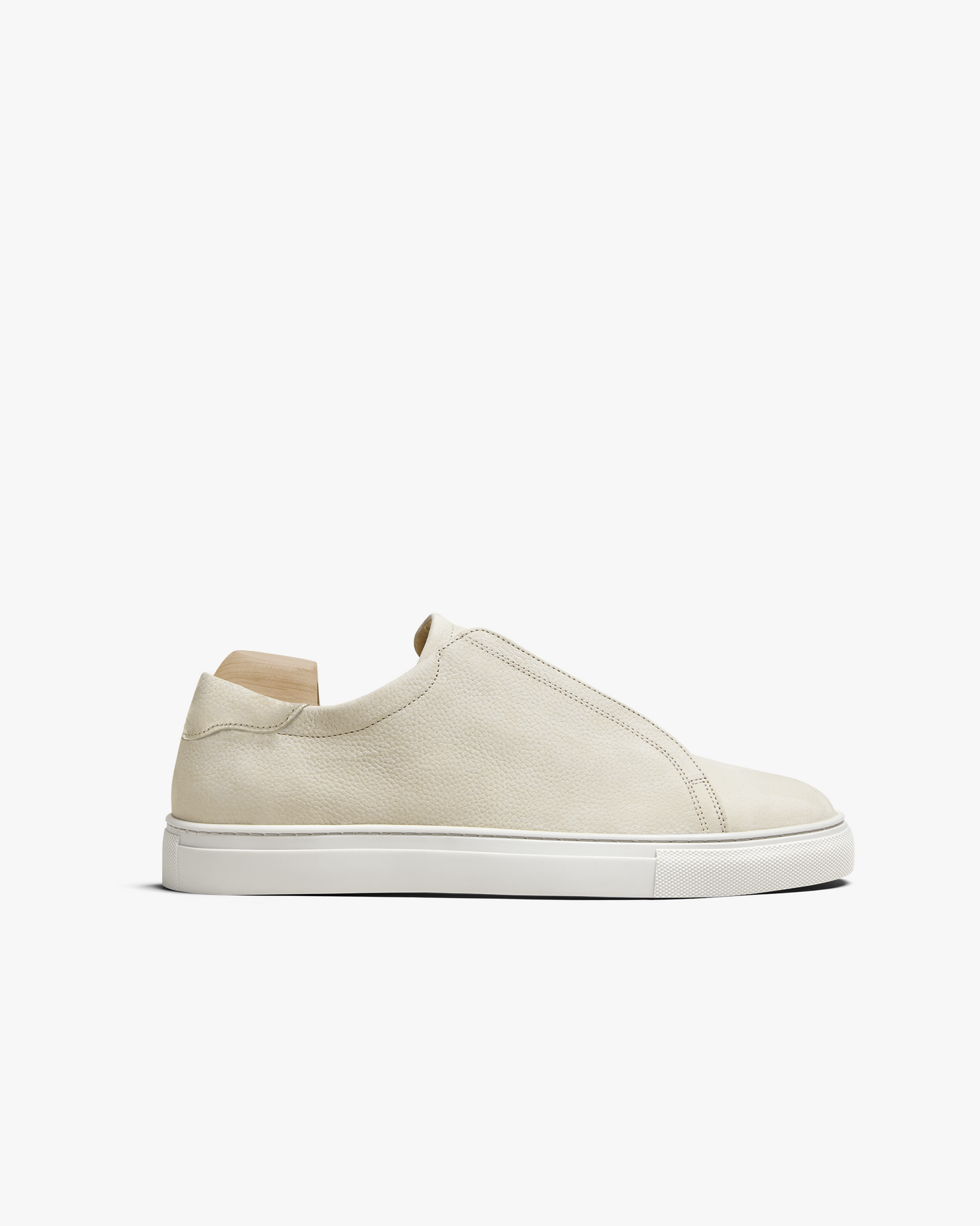 Side profile of Alnö – Beige Nubuck, a slip-on sneaker in tumbled leather with a clean white sole, on a shoe tree.