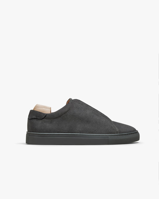 A side profile view of Alnö – Dark Grey Suede, showcasing its slip-on design, tonal sole, and suede upper.