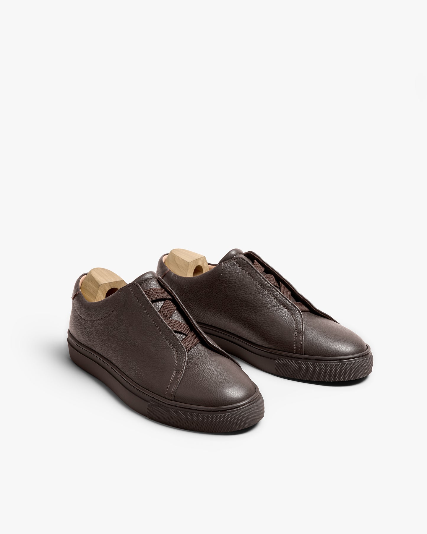 A pair of Alnö – Dark Brown Natural Grain sneakers with wooden shoe trees, shot against a white background.