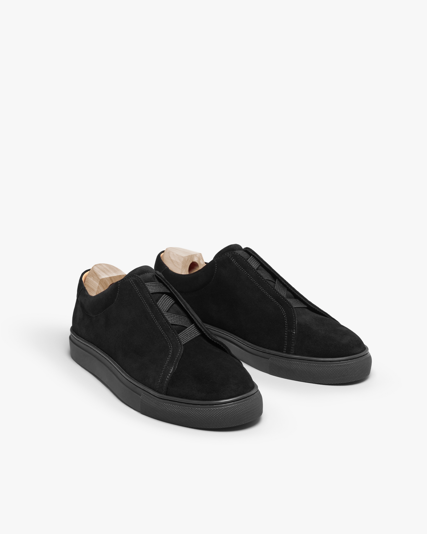 Alnö sneakers in black suede displayed at an angle, featuring soft suede uppers, M-shaped elastic bands across the instep, tonal soles, and wooden shoe trees for shape retention.