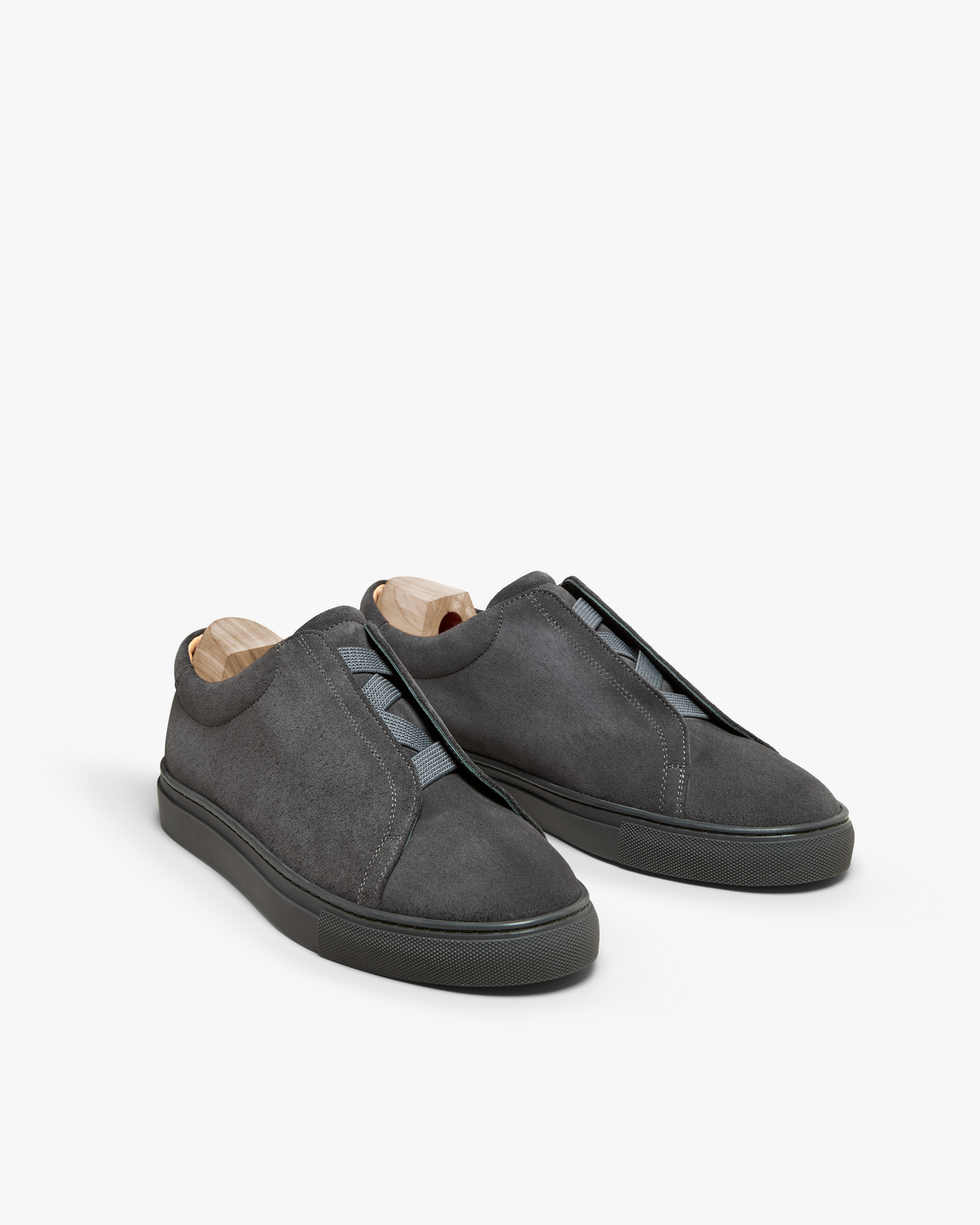A pair of Alnö – Dark Grey Suede sneakers with wooden shoe trees, shown against a white studio background.