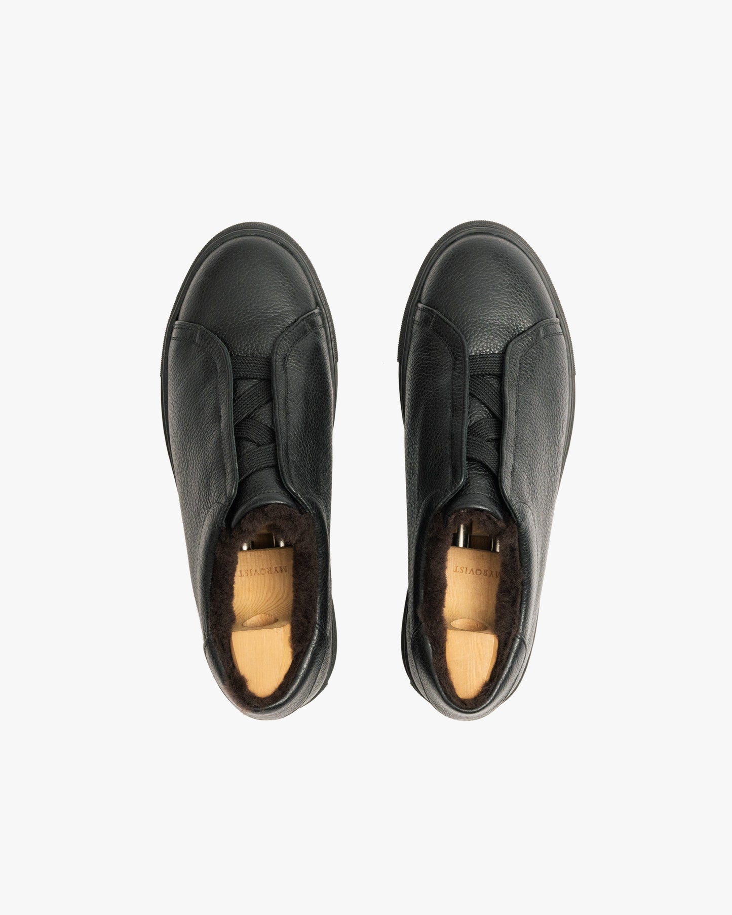 A top-down shot of a pair of Alnö Shearling – Black Natural Grain sneakers fitted with wooden shoe trees.