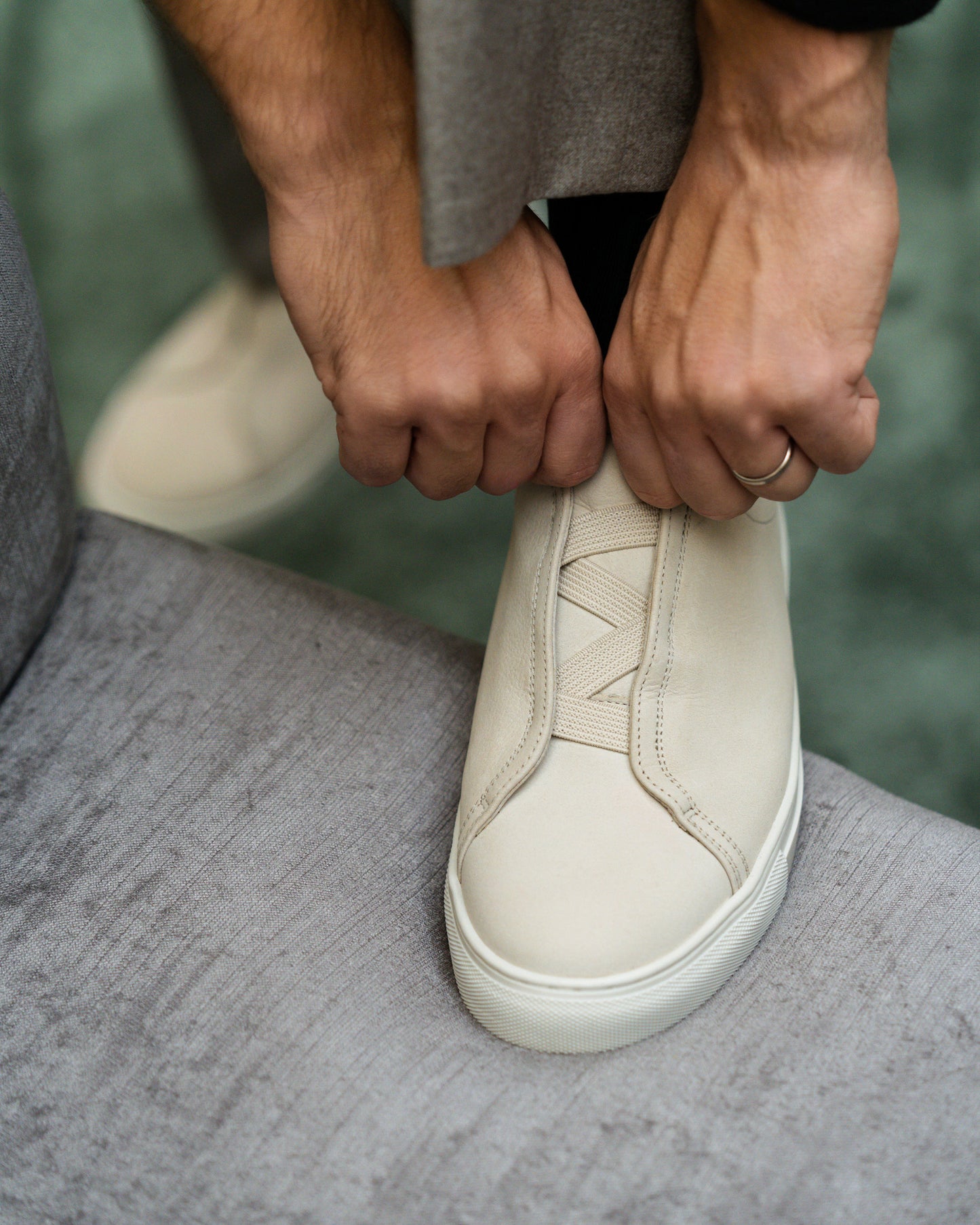 Person putting on a beige nubuck sneaker, with a focus on the hands and the elastic laces.