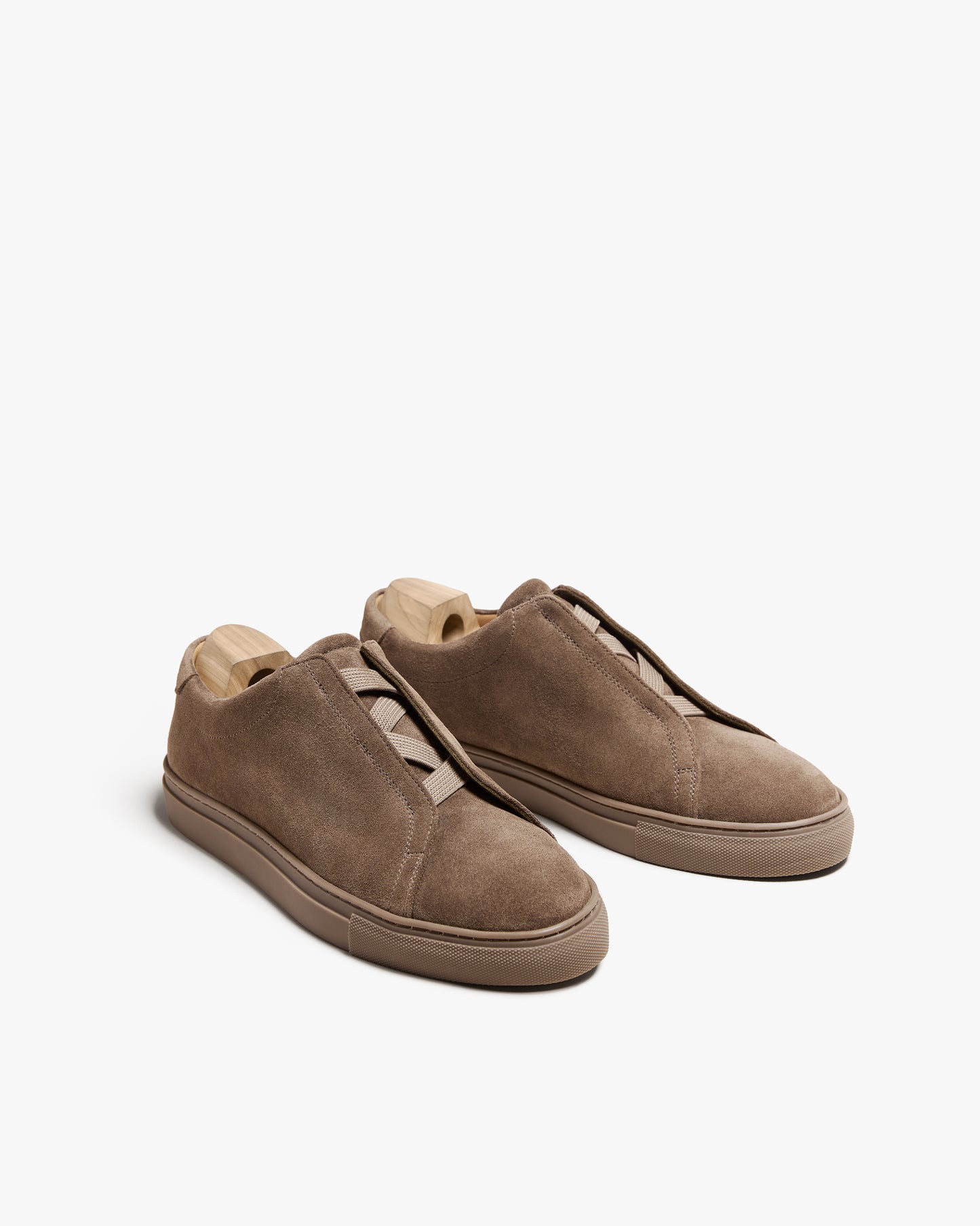 A pair of Alnö – Taupe Suede sneakers with wooden shoe trees, shot against a white background.