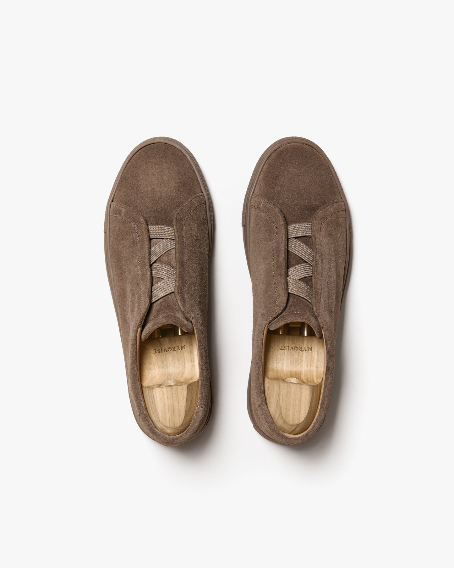 A top-down view of a pair of Alnö – Taupe Suede sneakers with wooden shoe trees, set against a plain white background.