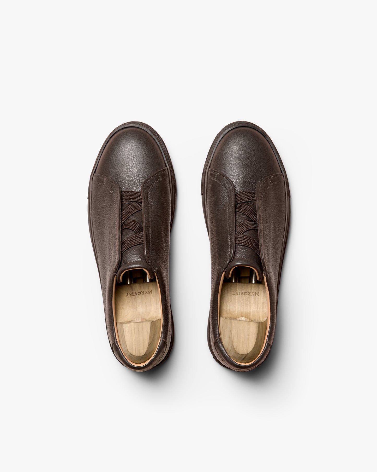 A pair of Alnö – Dark Brown Natural Grain sneakers with wooden shoe trees, shot from above on a white background.