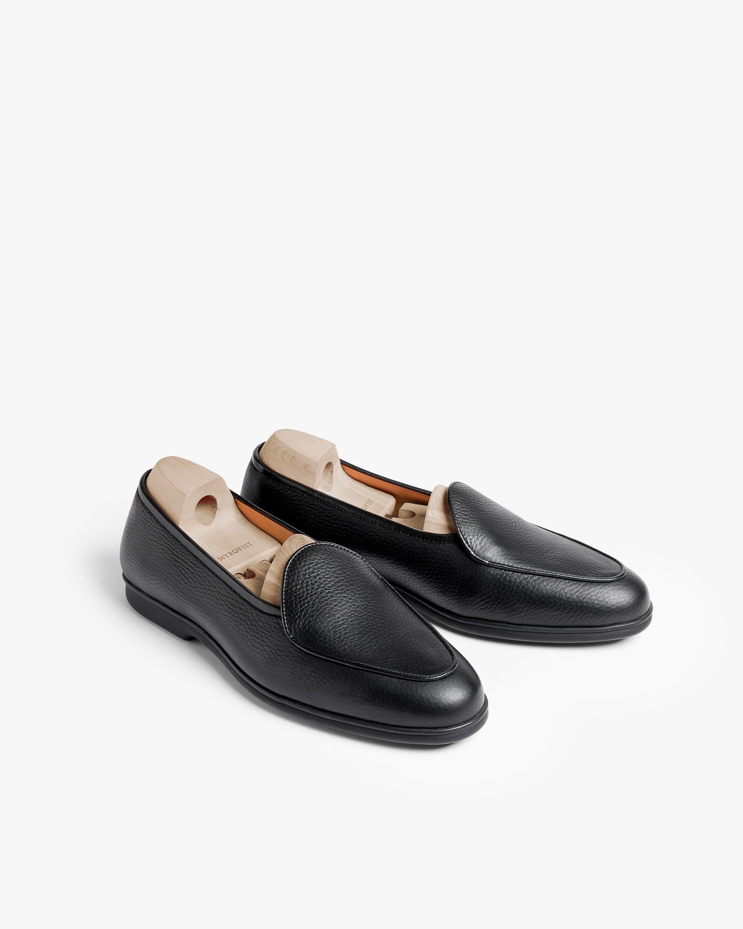 Ängby Walker in black grain calf shown as a pair with wooden shoe trees, highlighting the softly pebbled leather, minimalist silhouette, and gently rounded toe on a clean white background.