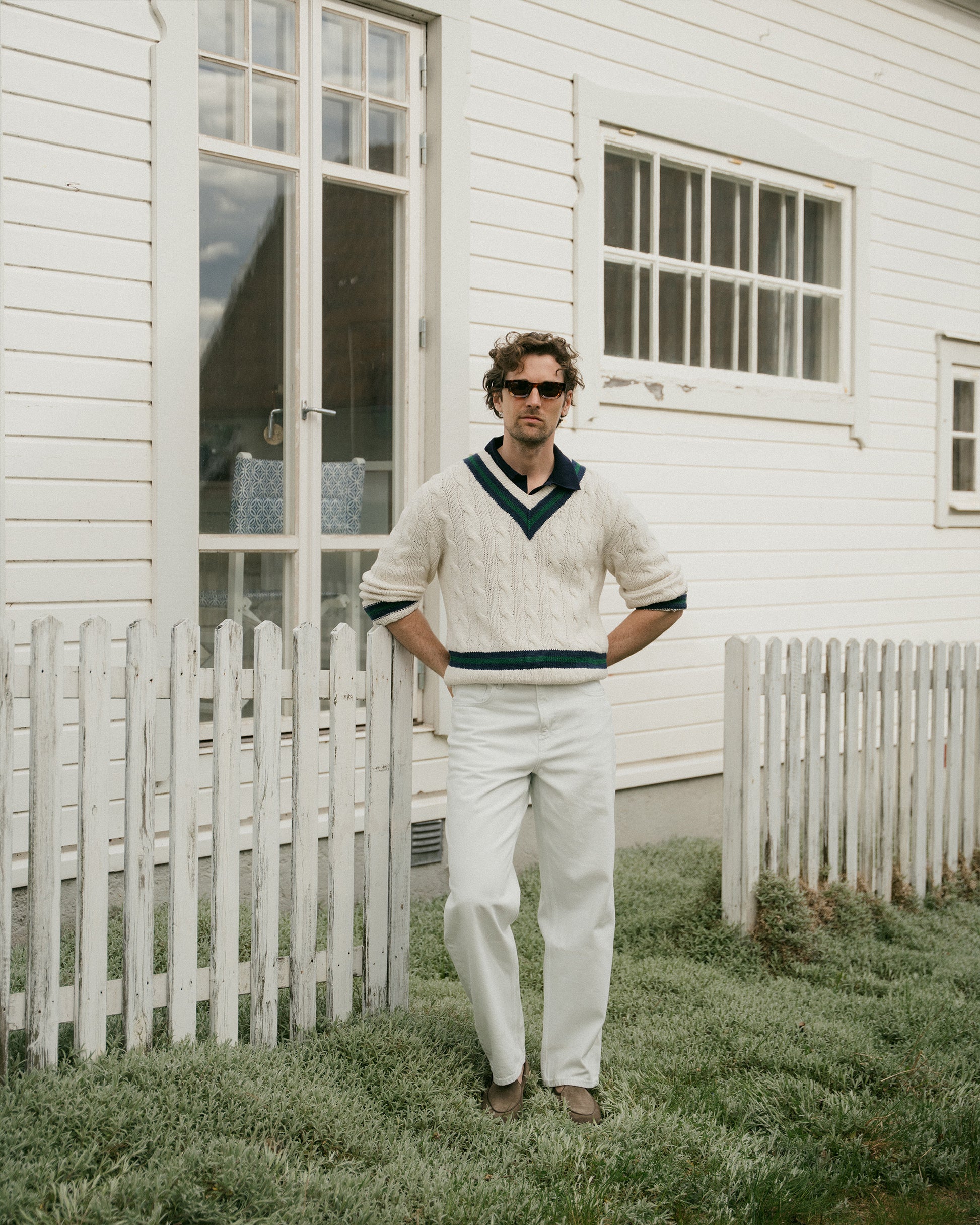 Man in a cream cricket sweater and white trousers wearing Ängby – Taupe Suede loafers, standing in front of a white house.
