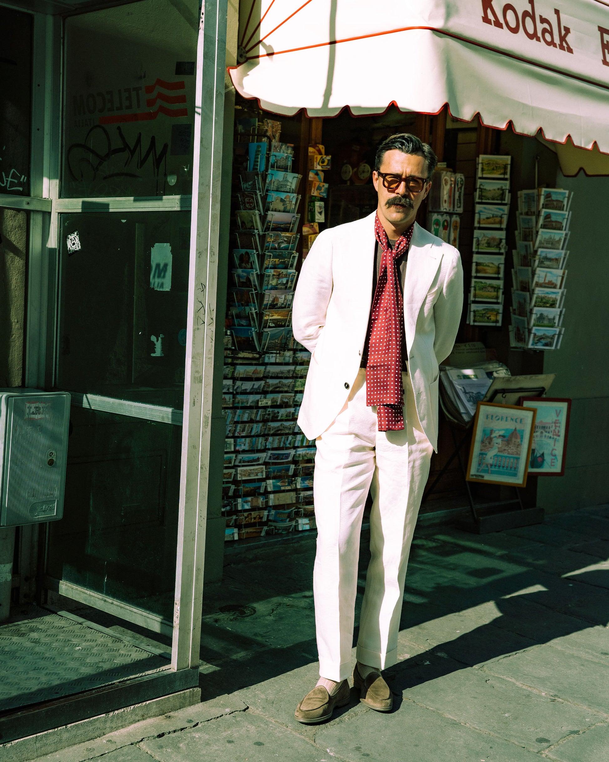 A man wearing a white suit and red scarf, styled with Ängby Walker – Taupe Suede loafers on a city sidewalk.