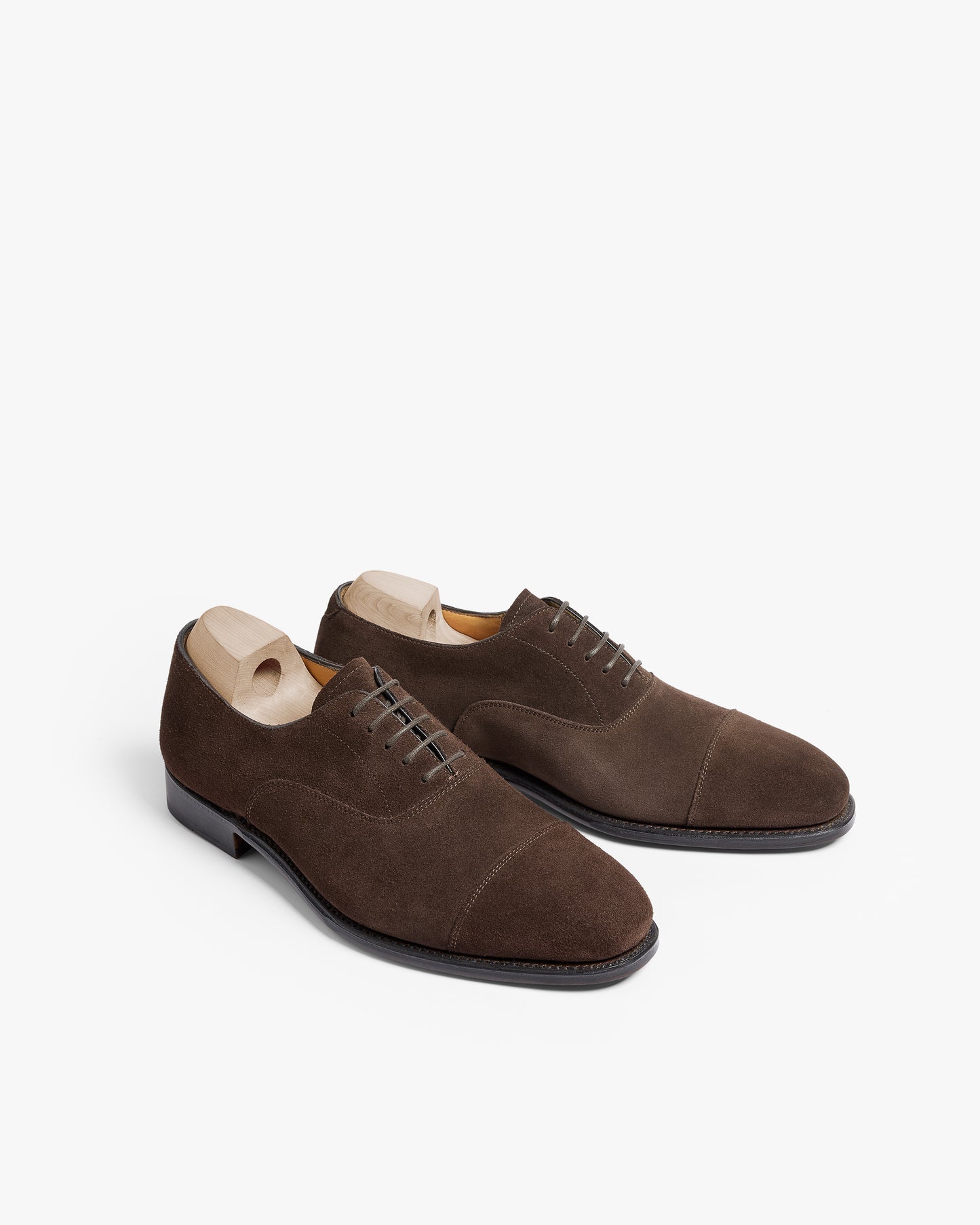 Äppelviken II in dark brown suede displayed at an angle, featuring a classic cap-toe oxford silhouette with closed lacing, soft suede texture, and wooden shoe trees inside each shoe.