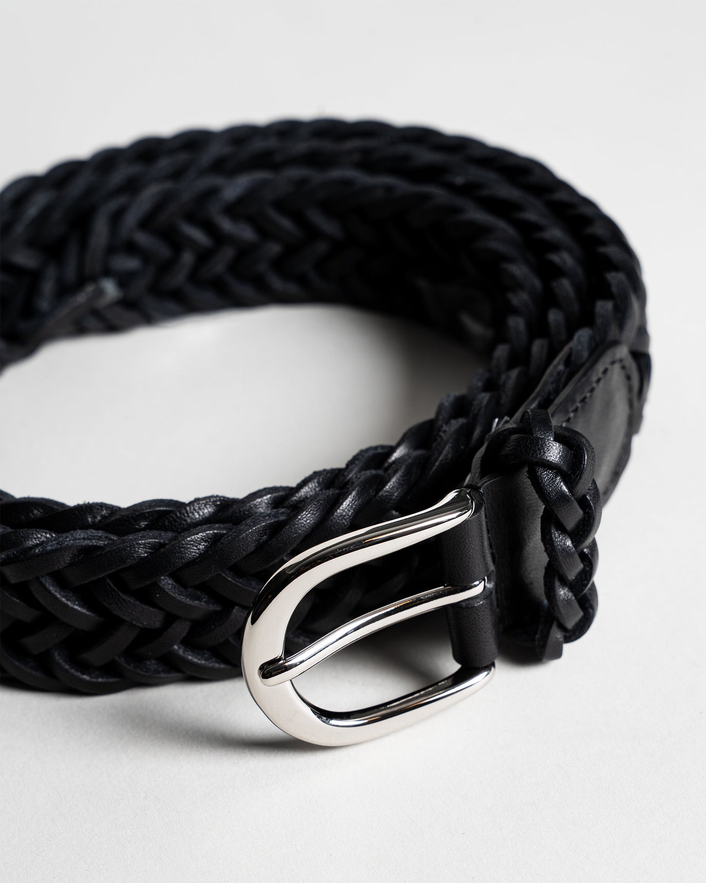 A close-up shot of Belt – Braided Black Leather, coiled to showcase the intricate weave and the polished silver buckle.