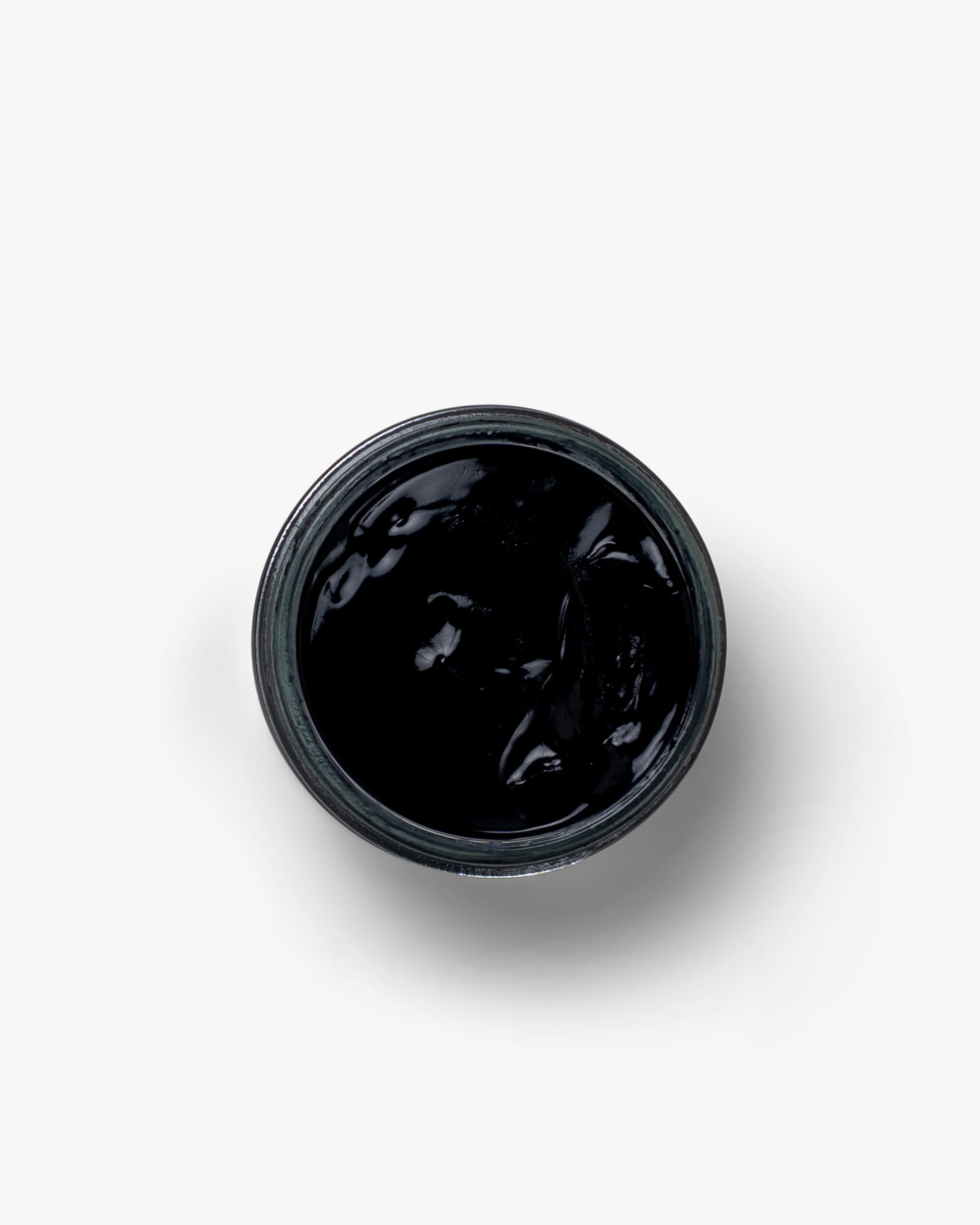 A top-down view of an open jar of Myrqvist black shoe cream against a white background, highlighting its rich texture.