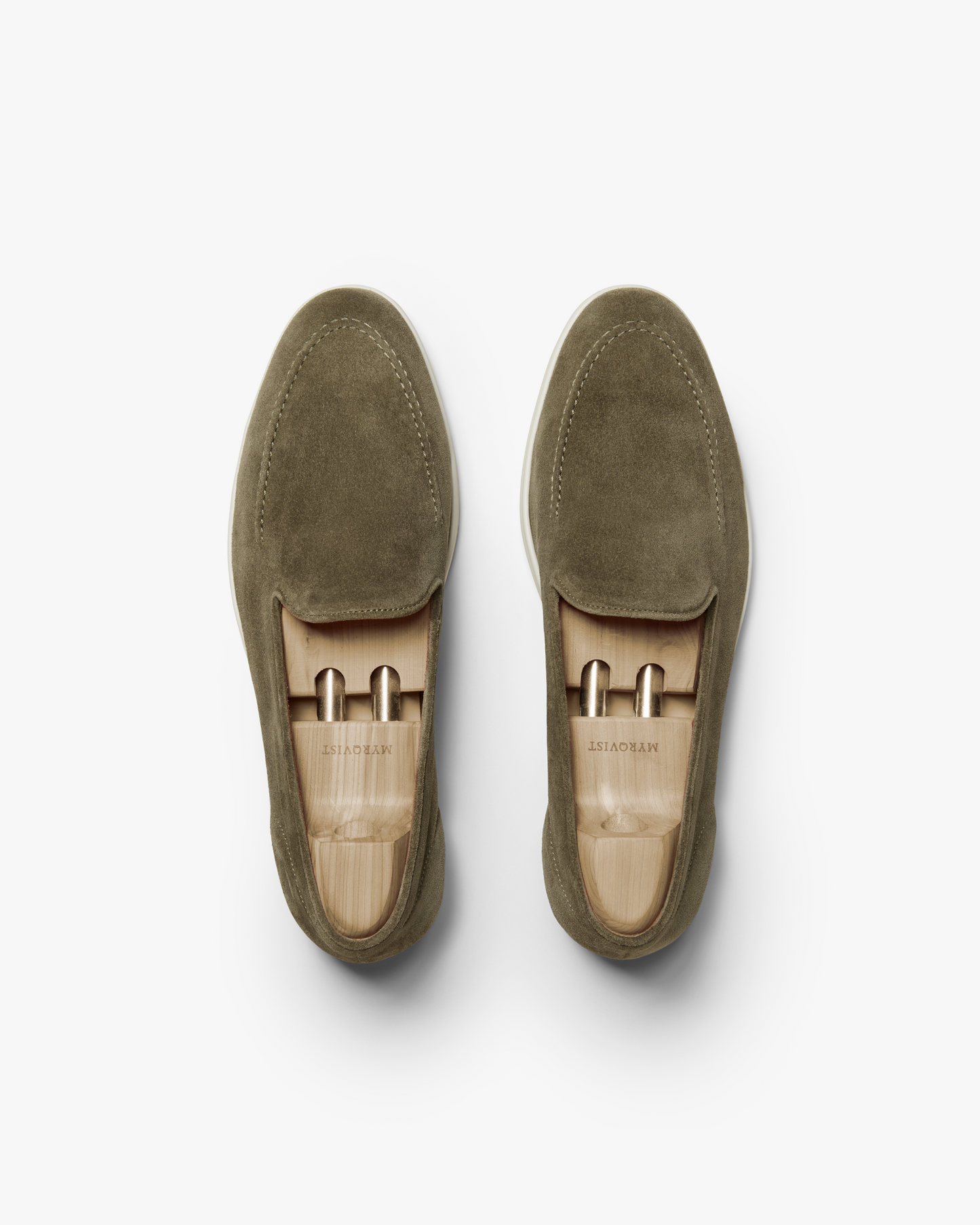 An overhead studio shot of Brännö II – Moss Green Suede loafers, fitted with wooden shoe trees on a white background.