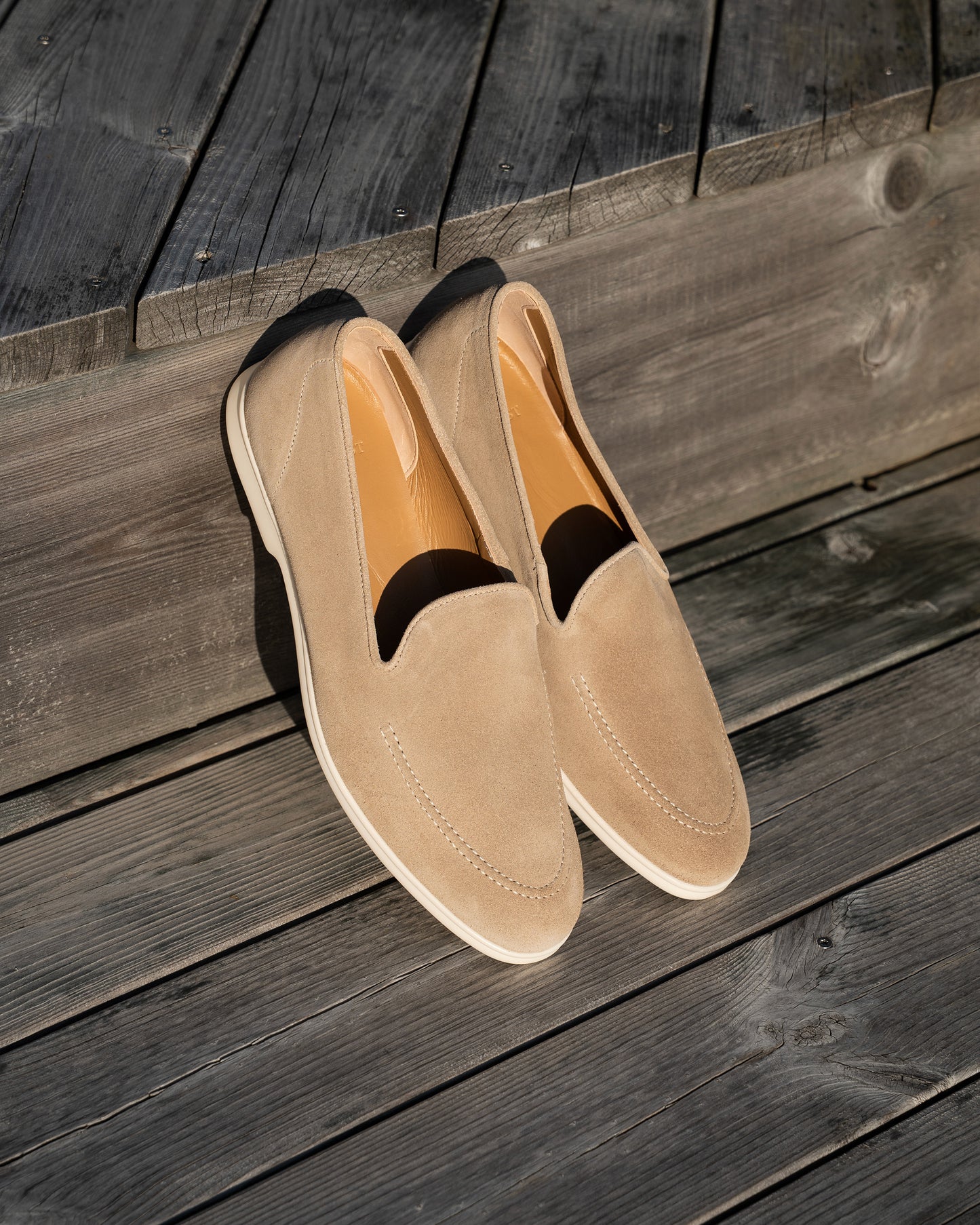 Brännö II – Sand Suede loafers displayed on a sunlit, dark wooden deck.