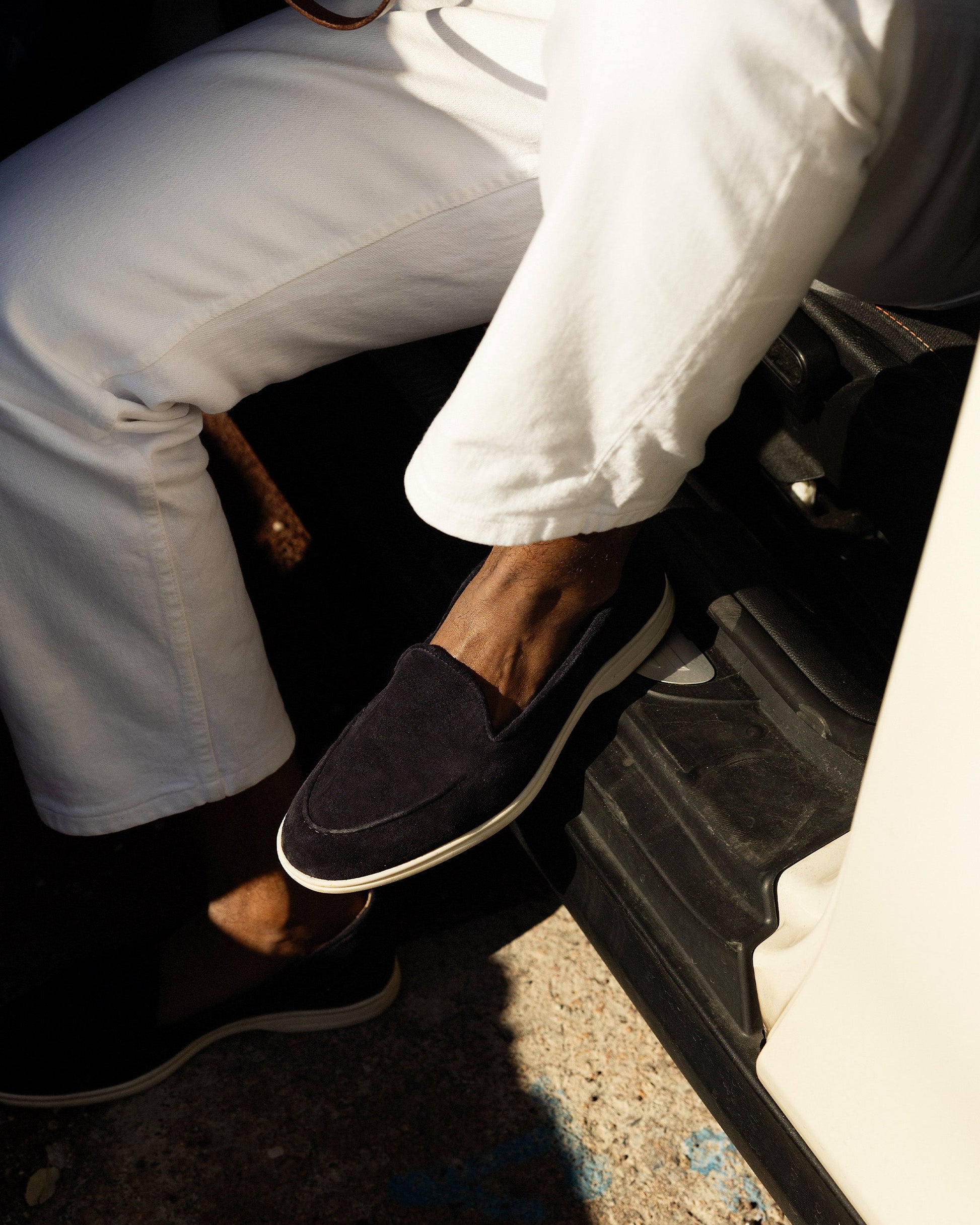 Close-up on a person wearing Brännö II – Navy Suede loafers with white trousers.