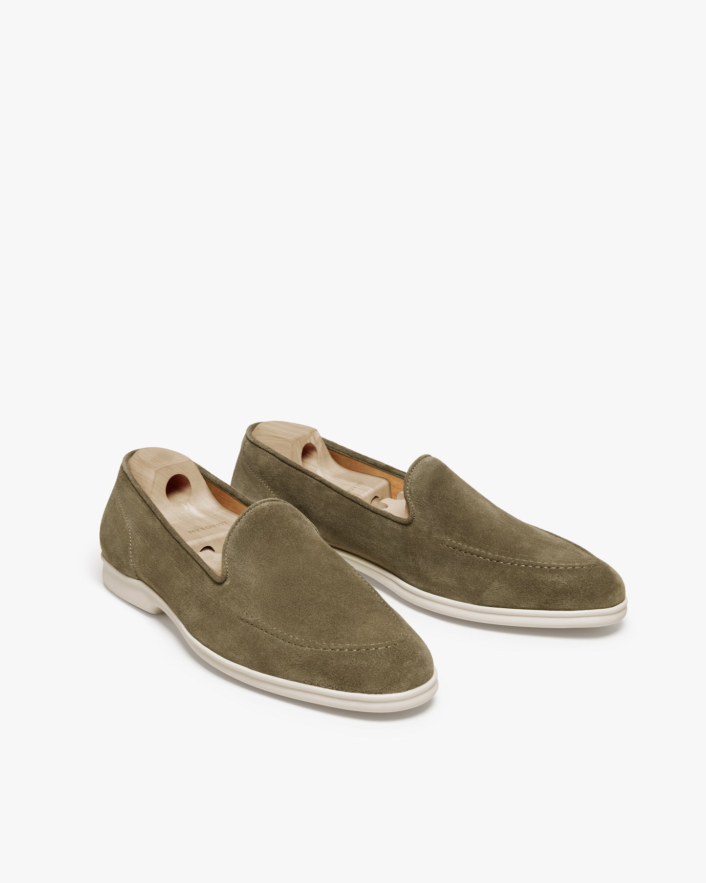A pair of Brännö II – Moss Green Suede loafers with wooden shoe trees on a white background.