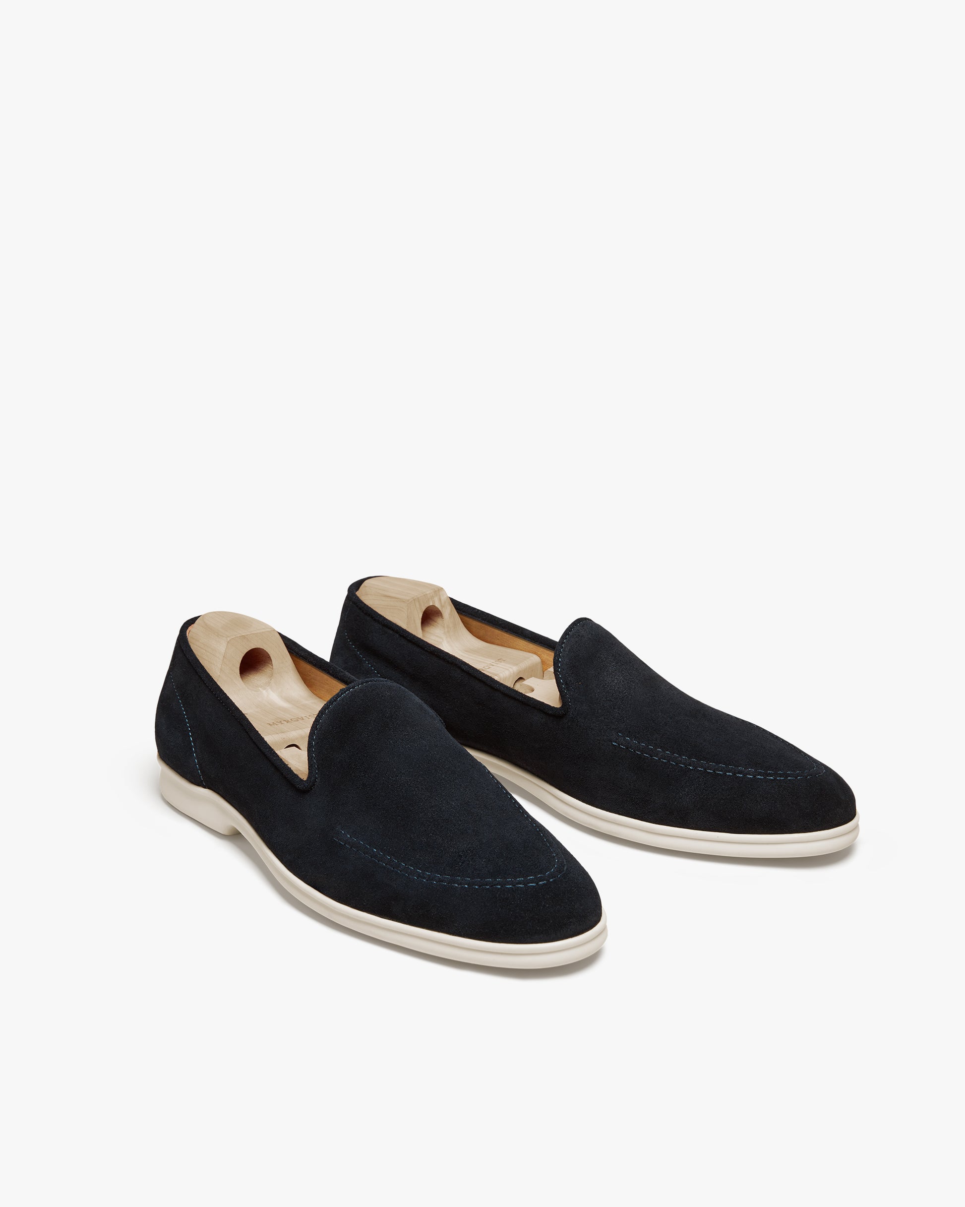 A pair of Brännö II – Navy Suede loafers with wooden shoe trees inside, shot against a white background.