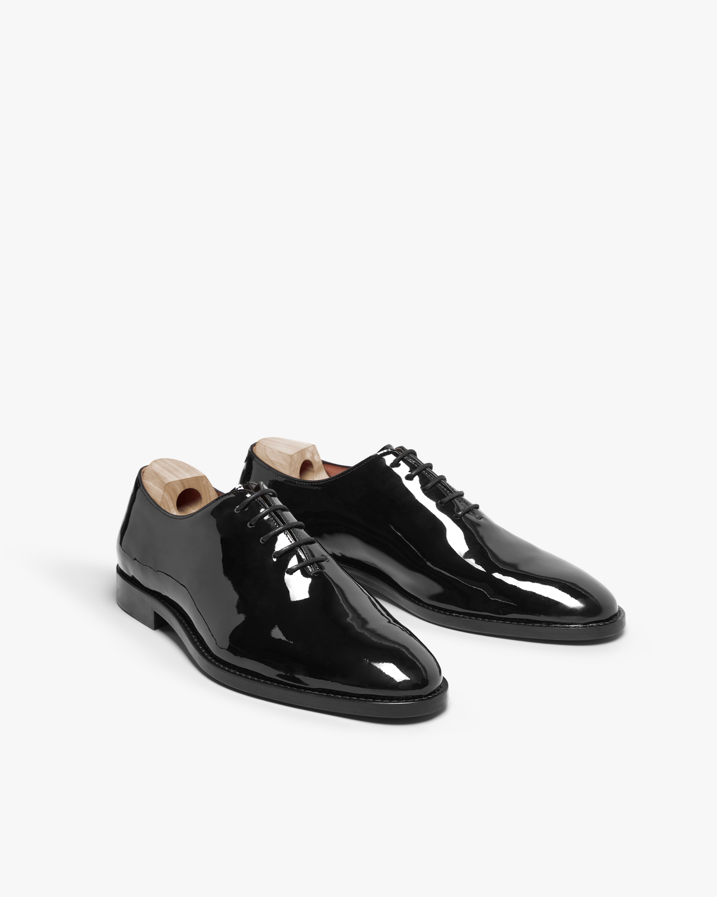 A pair of Drottningholm – Black Patent Leather whole-cut Oxfords with a high-gloss finish, shot against a white background.