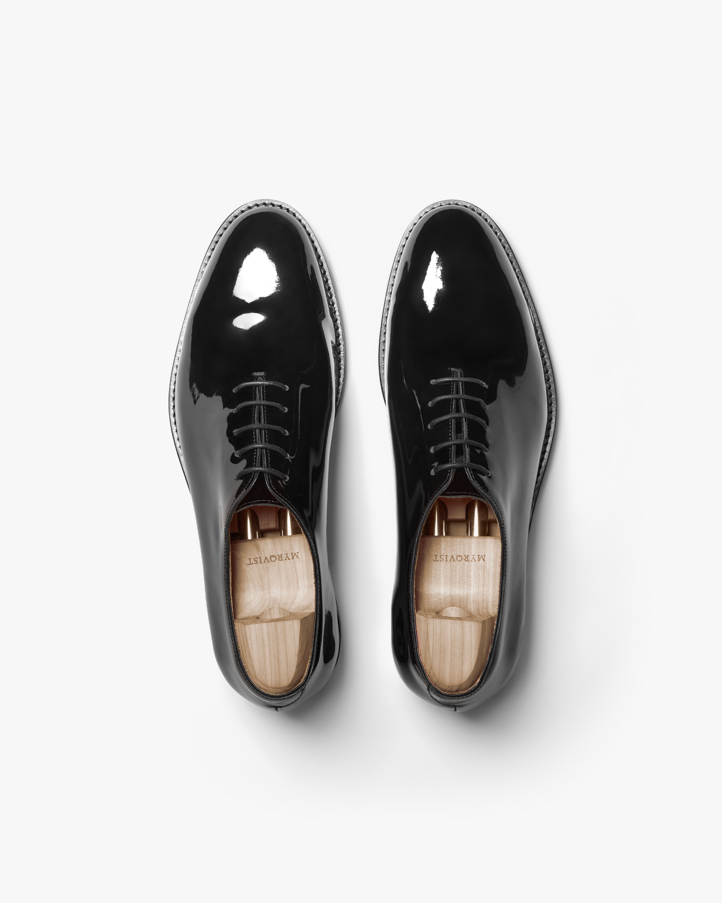 Top-down view of Drottningholm – Black Patent Leather Oxfords with wooden shoe trees on a white background.