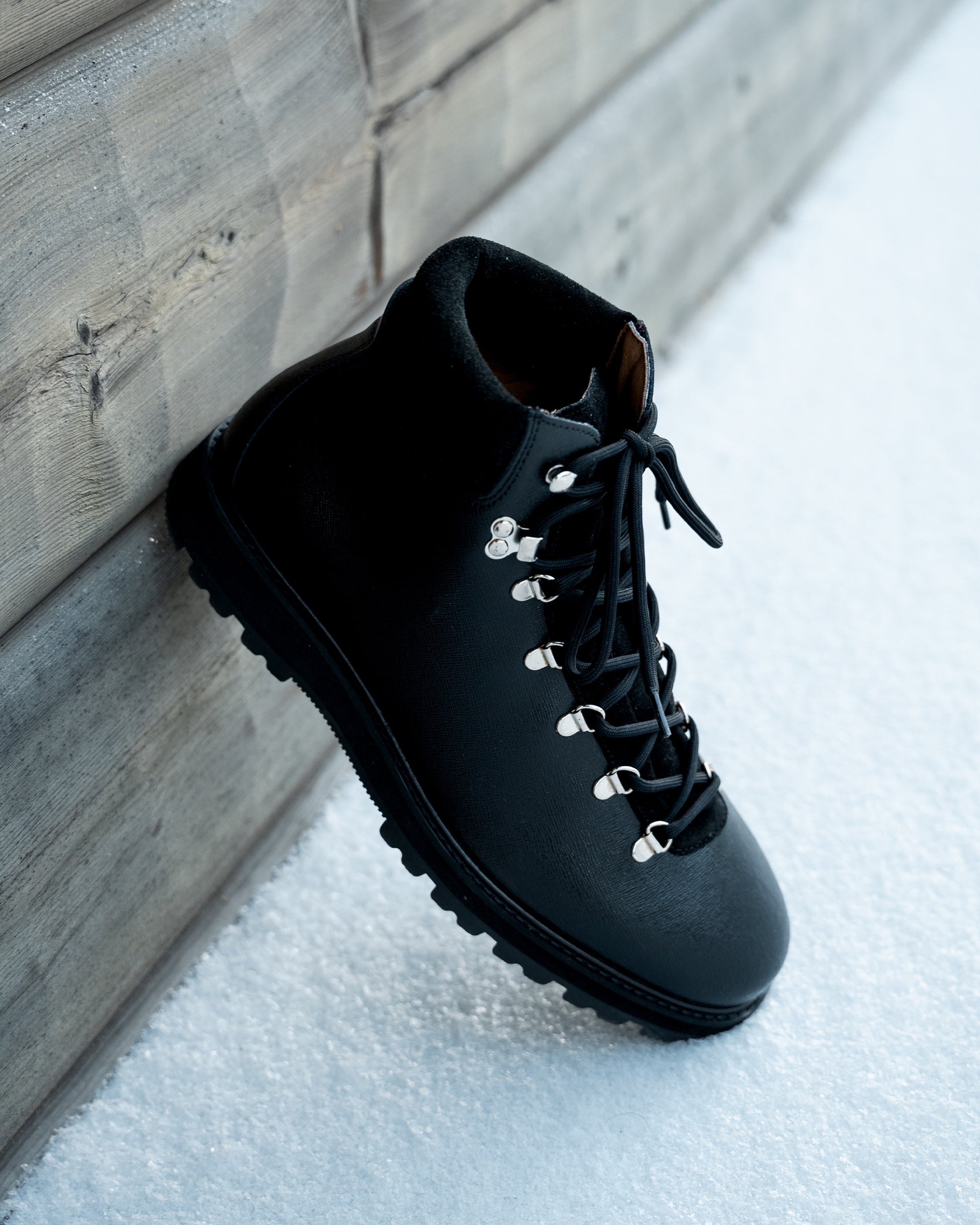 A Duved II – Black Grain Calf boot resting against a wooden wall in the snow.