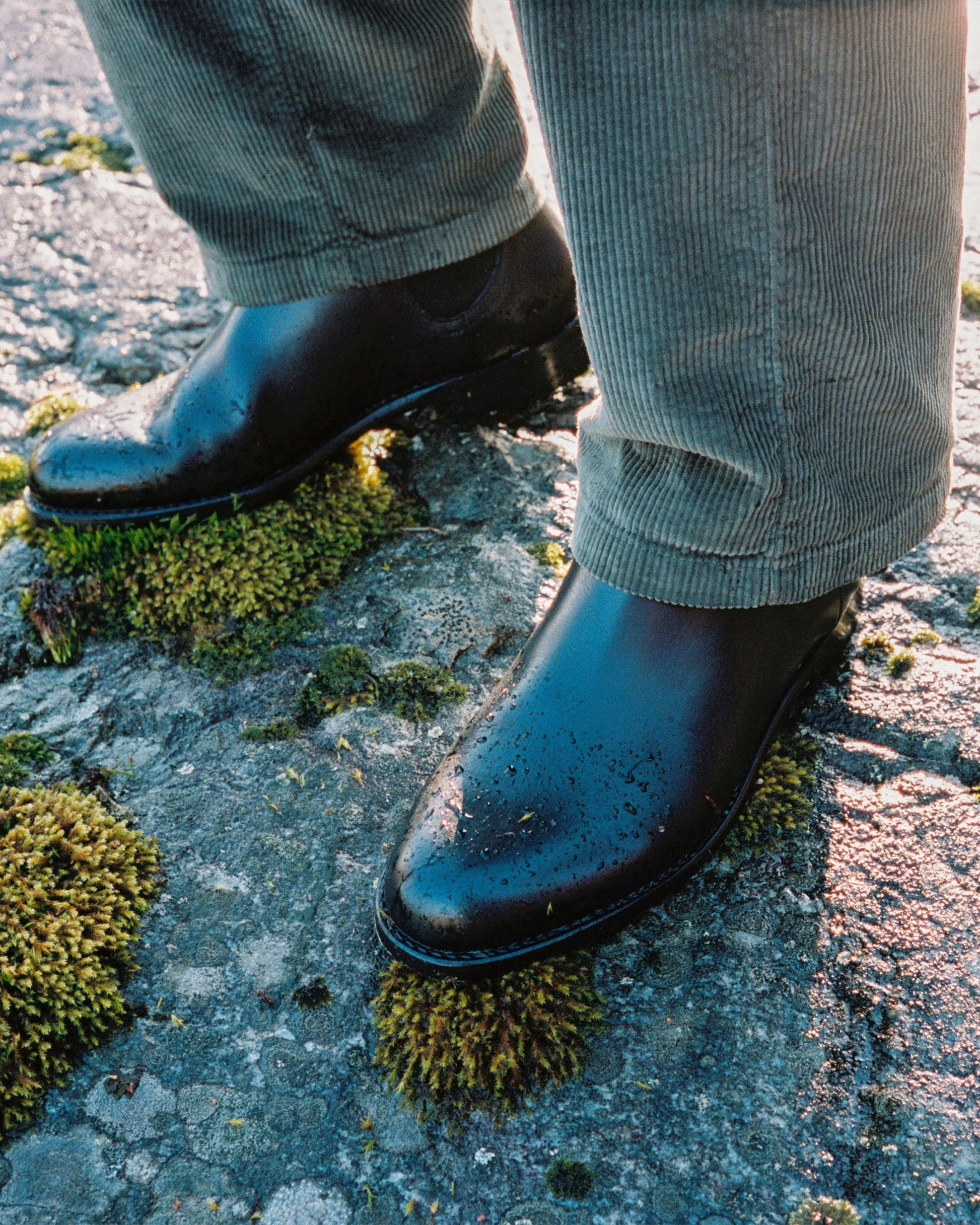 Close-up of Elfvik – Dark Brown Calf boots paired with corduroy trousers, standing on a moss-covered rock.
