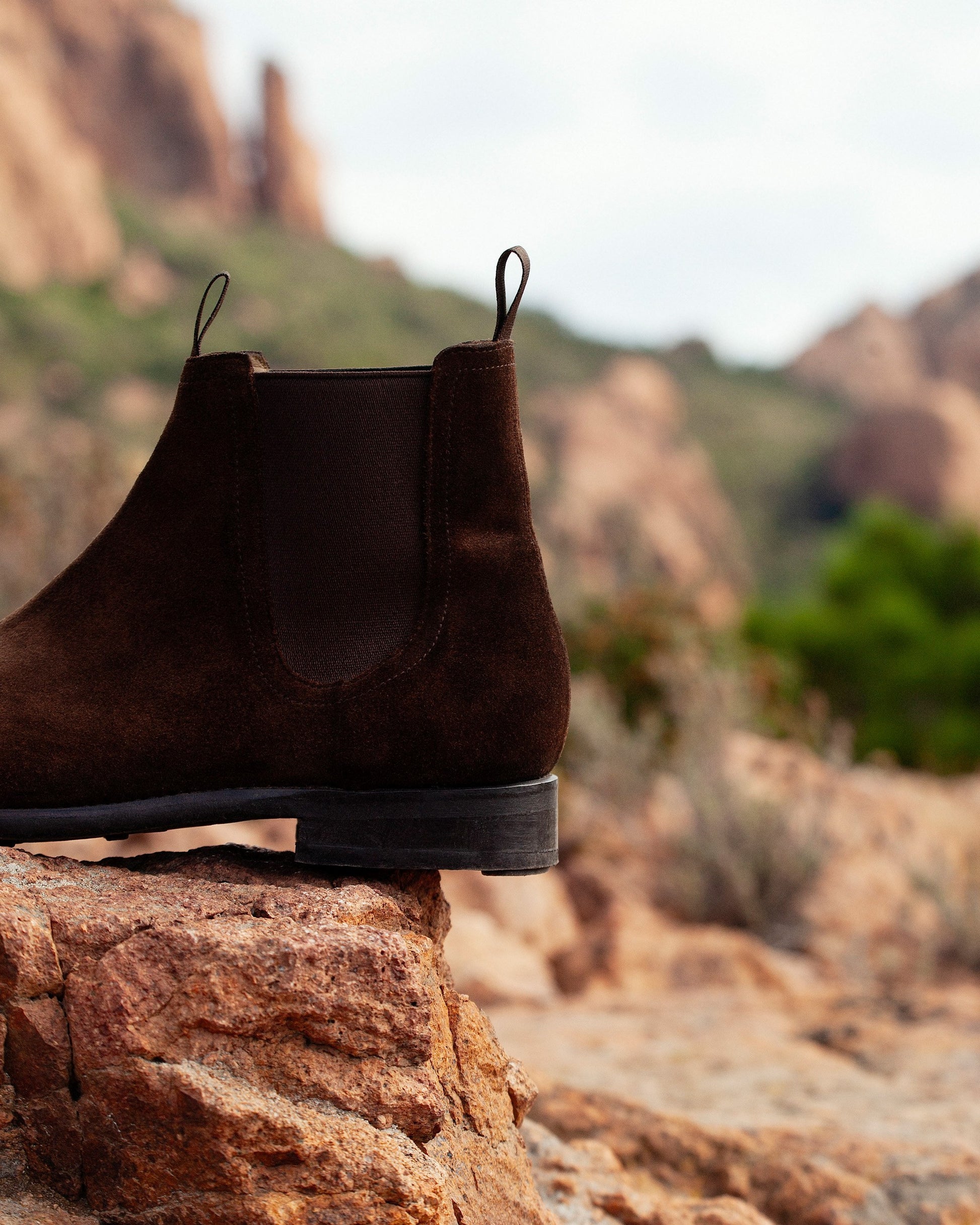Close-up of the Elfvik – Dark Brown Suede boot, detailing the side profile and heel on a rock in a rugged landscape.