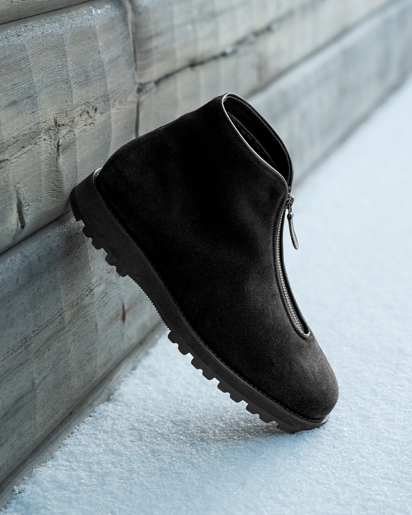Side profile of a Funäs – Black Suede boot leaning against a wooden wall in the snow.