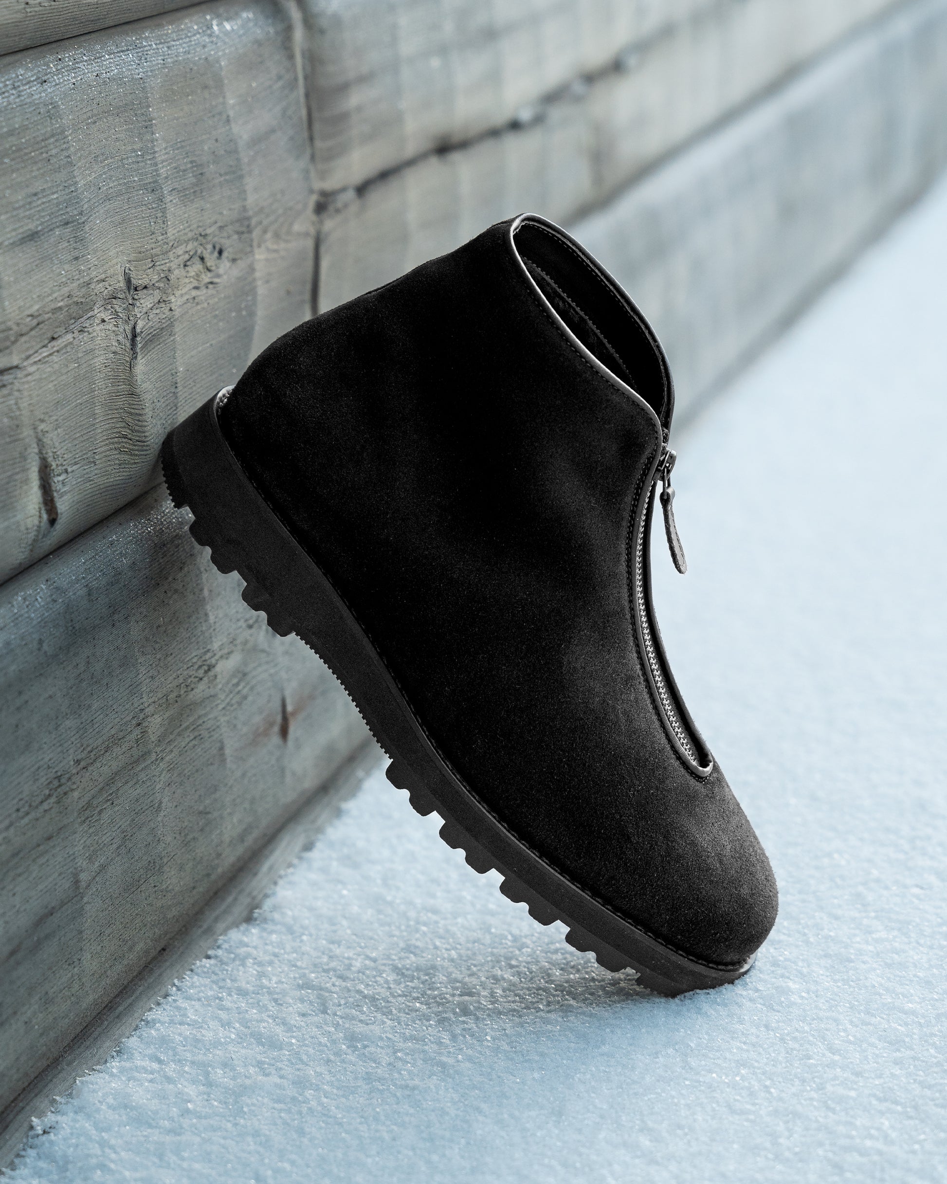 Side profile of a Funäs – Black Suede boot leaning against a wooden wall in the snow.