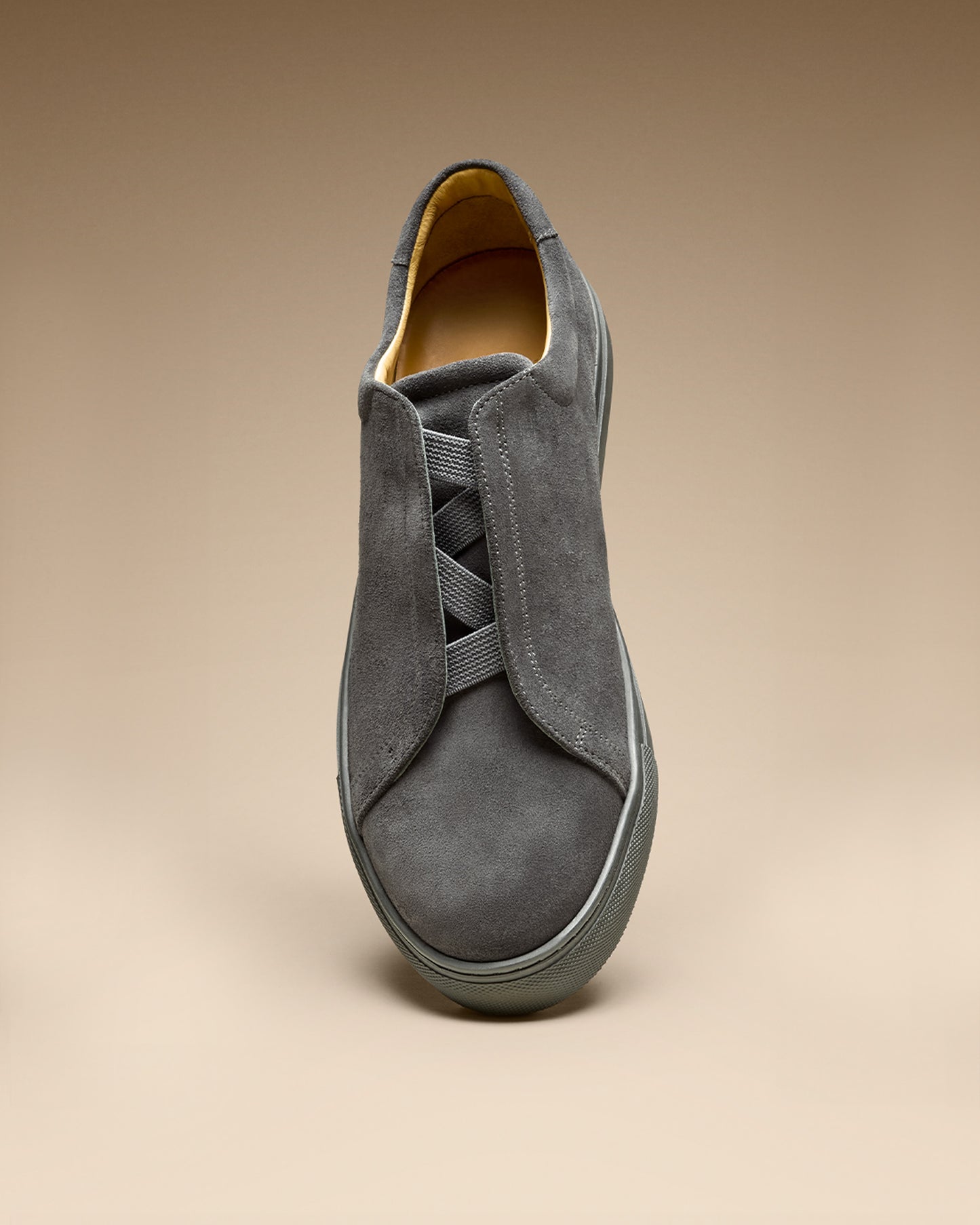 A close-up, front-facing view of the Alnö – Dark Grey Suede sneaker, highlighting its signature M-shaped elastic detail.