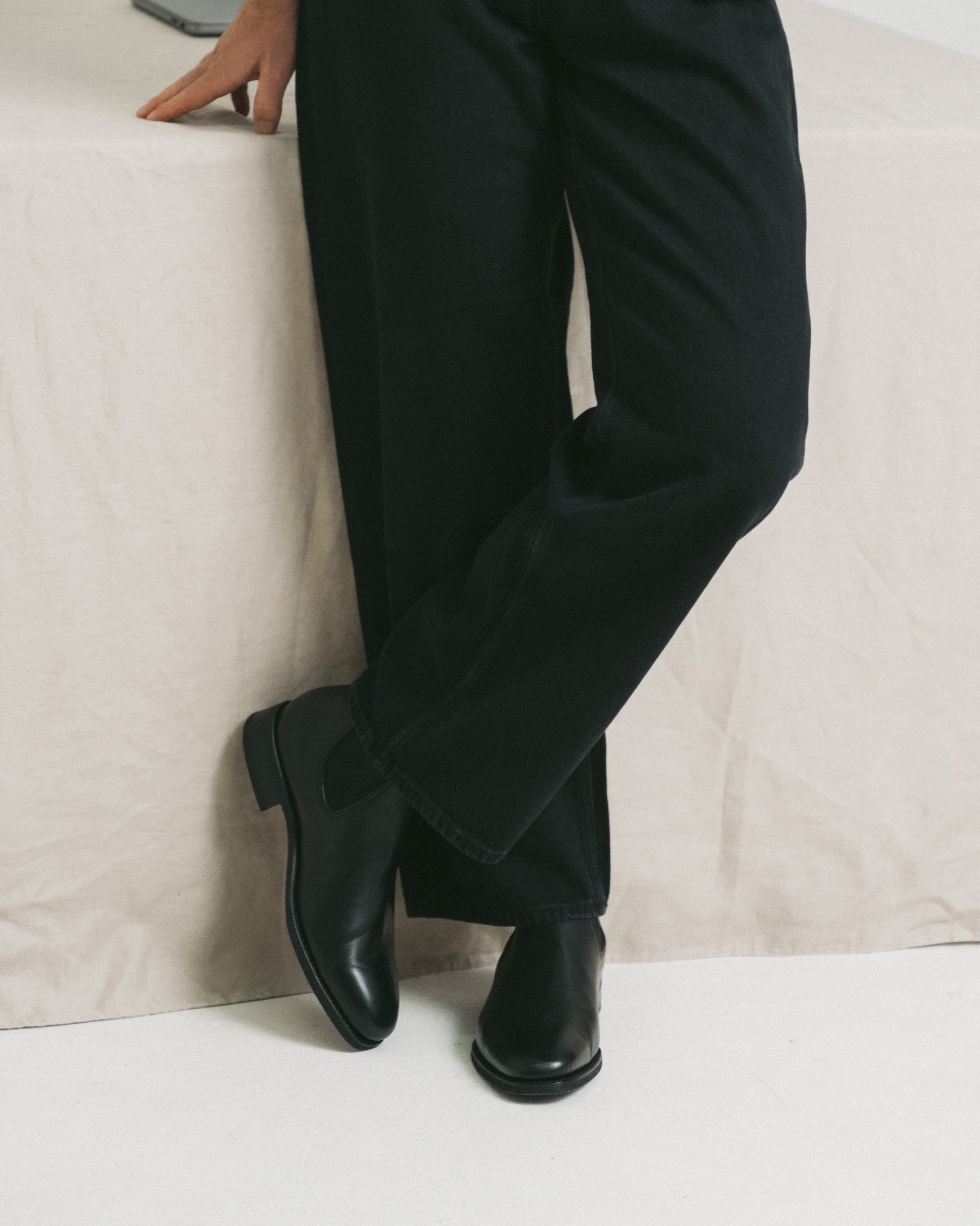A person stands with their legs crossed, wearing black trousers and Granhult – Black Calf Chelsea boots.