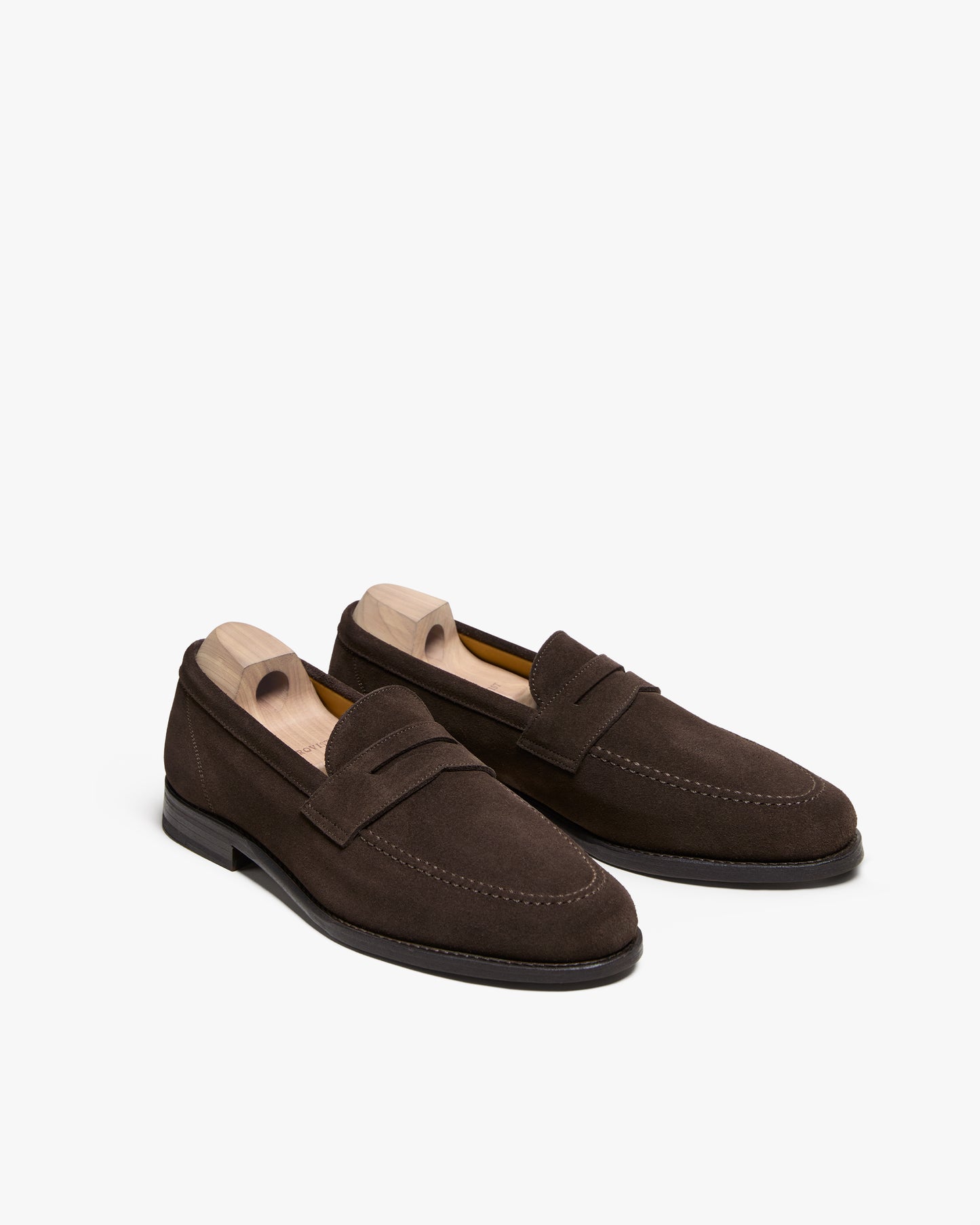 A pair of Lysekil II – Dark Brown Suede penny loafers with wooden shoe trees, set against a white background.