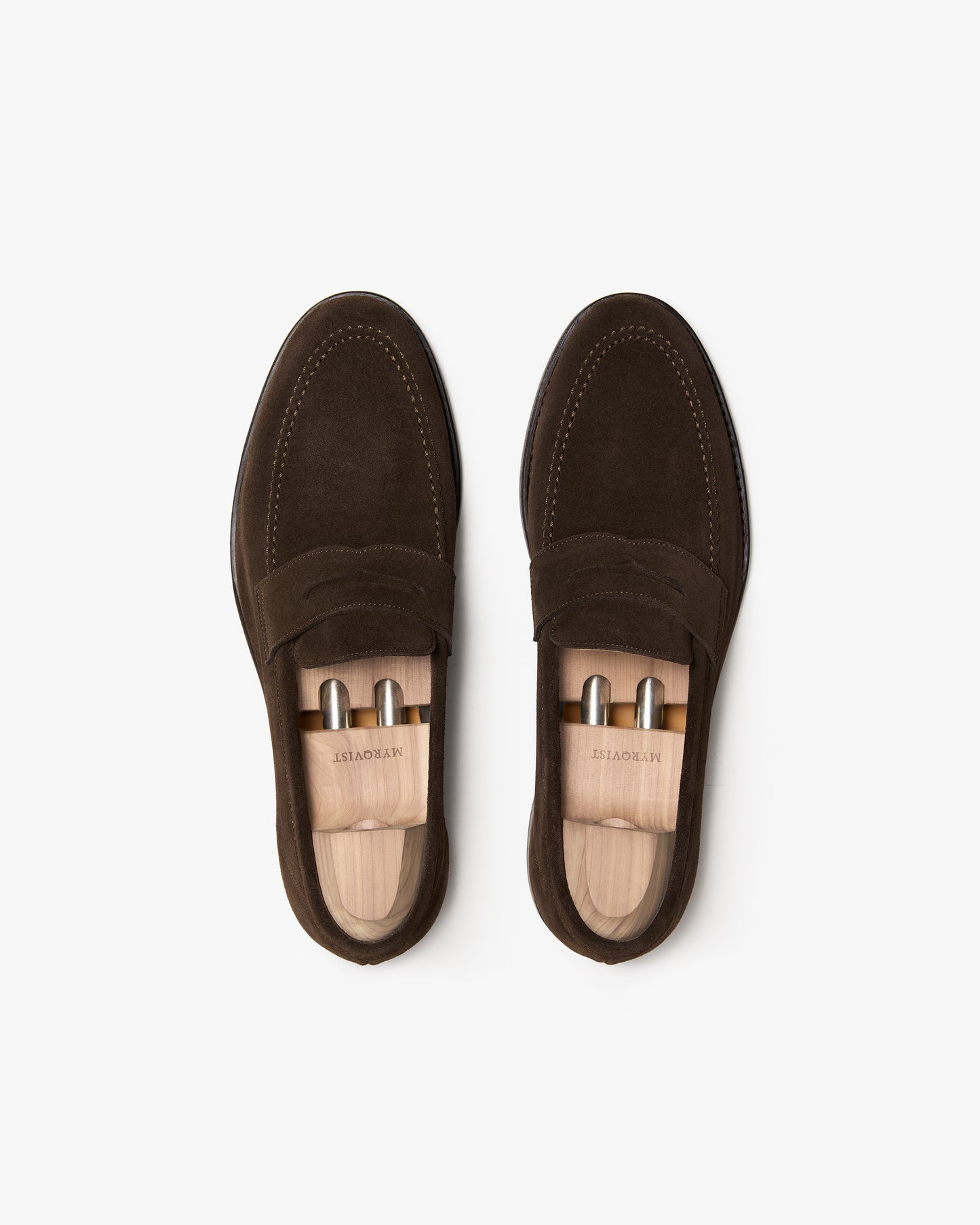 A pair of Lysekil II – Dark Brown Suede loafers with wooden shoe trees, seen from above on a white background.