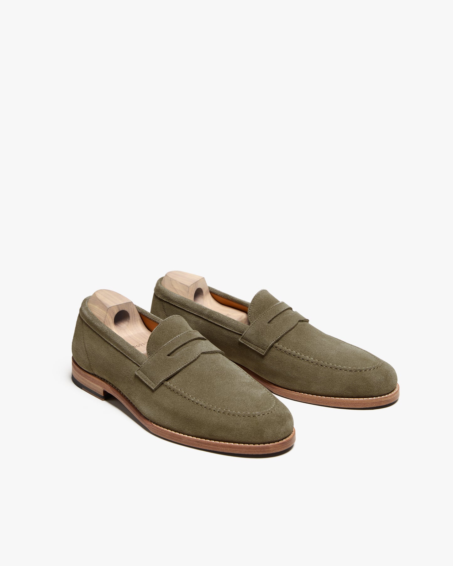Studio shot of a pair of Lysekil II – Green Suede loafers with shoe trees, angled on a white background.