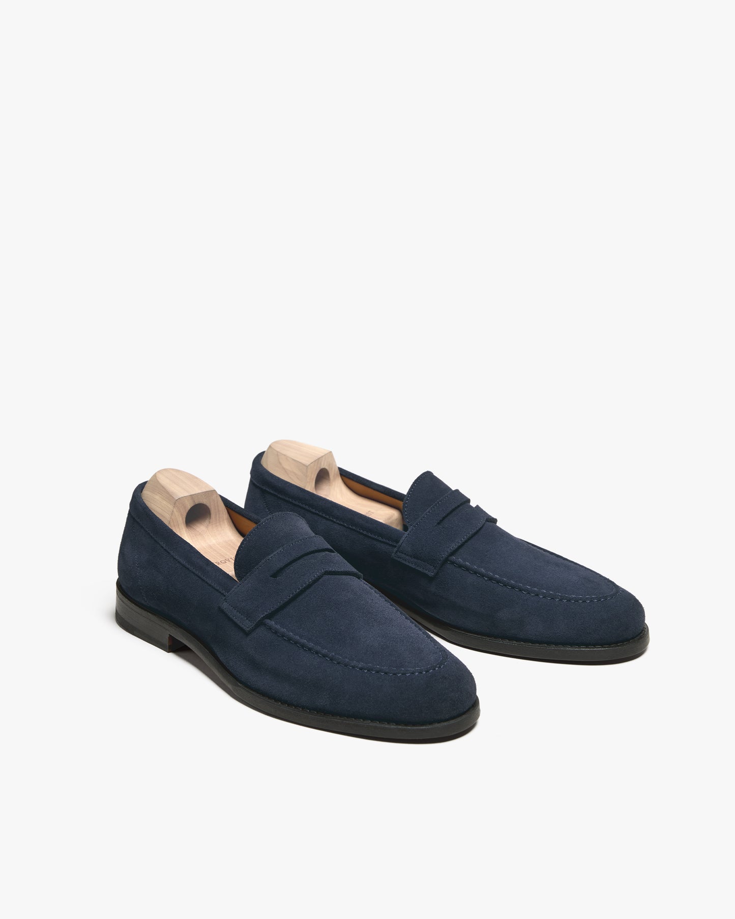 A pair of Lysekil II – Navy Suede penny loafers with wooden shoe trees, against a white background.
