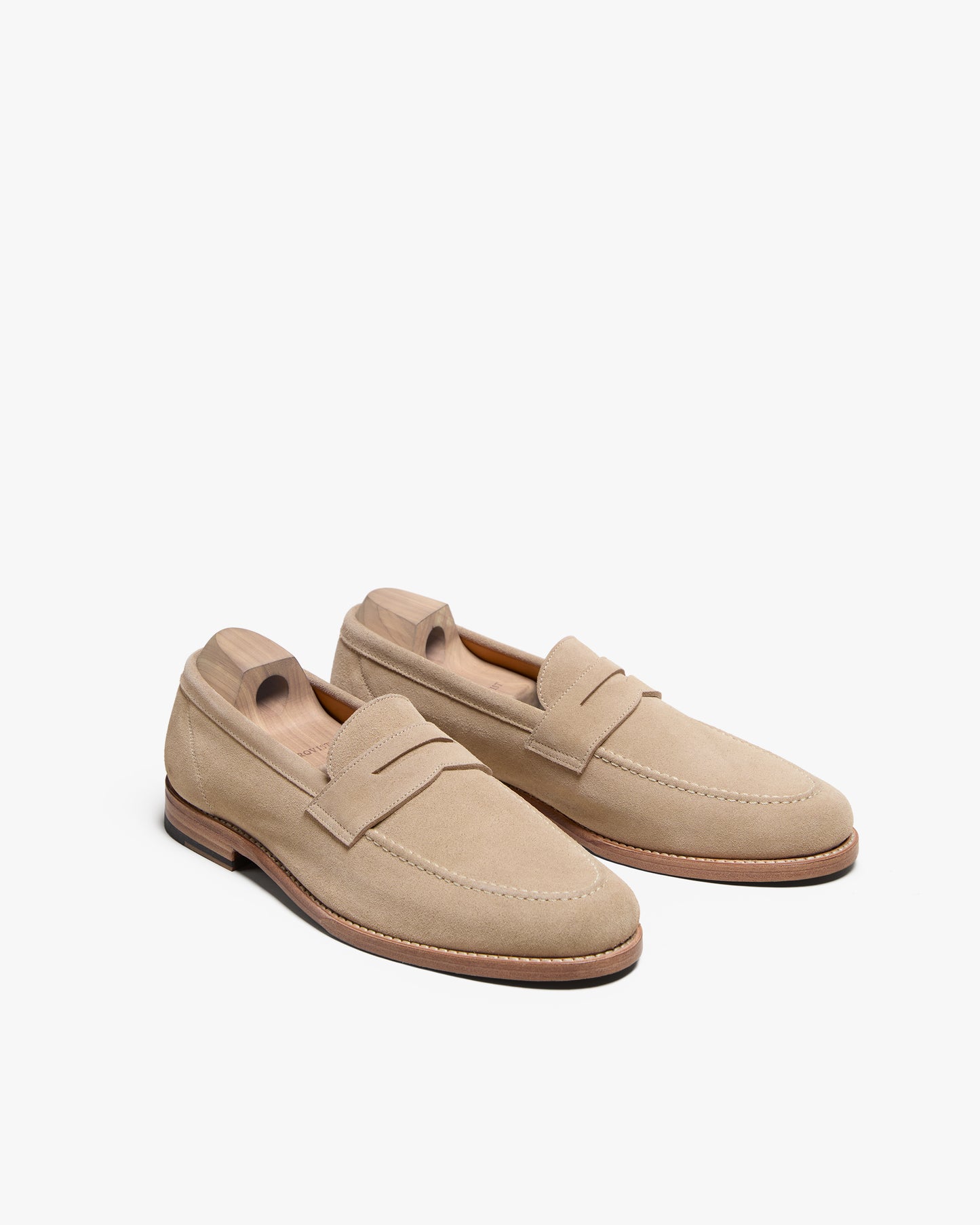 A pair of Lysekil II – Sand Suede loafers with wooden shoe trees on a white background.