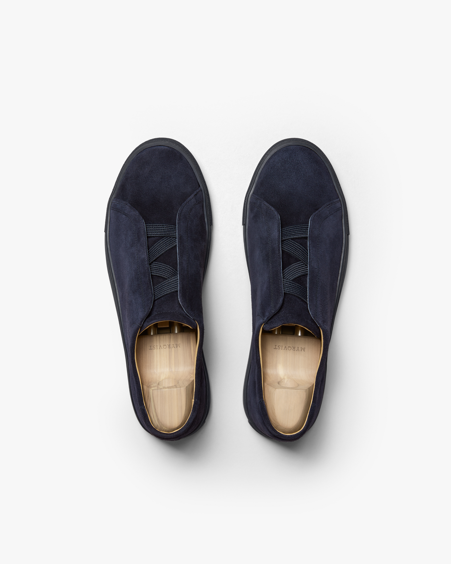 A flat lay of Alnö – Midnight Blue Suede sneakers with wooden shoe trees, highlighting the signature M-shaped elastics.