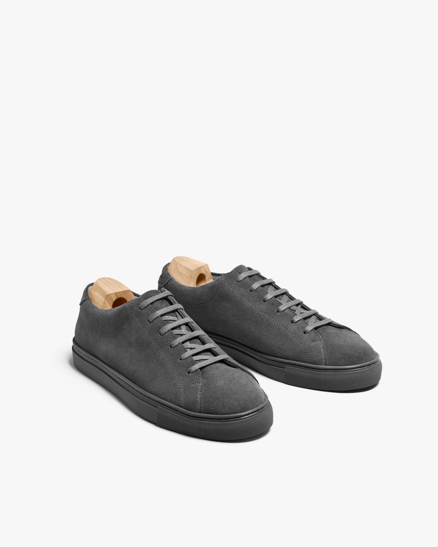 A pair of Oaxen Monochrome II – Dark Grey Suede sneakers with wooden shoe trees against a clean white background.
