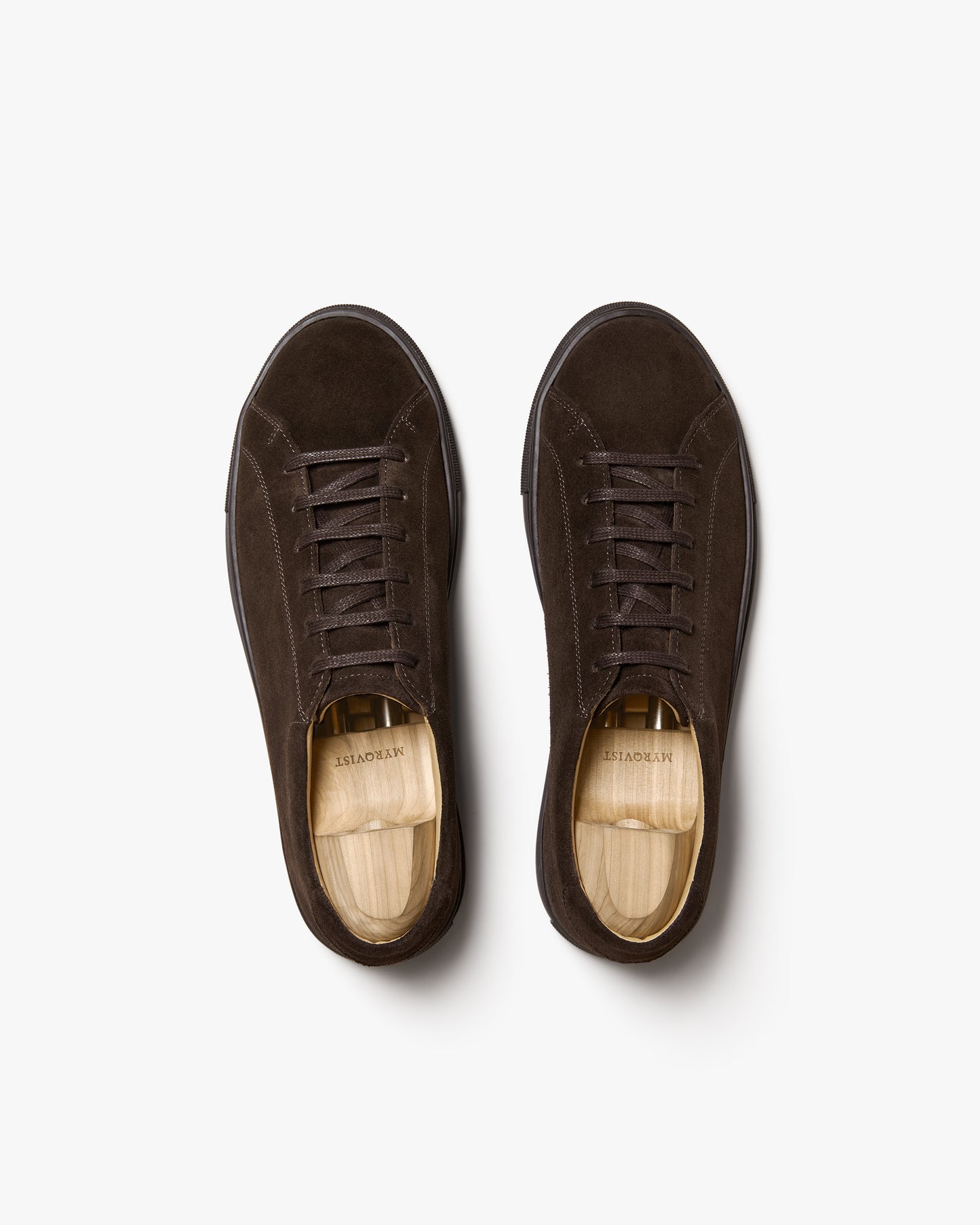 A top-down product shot of Oaxen Monochrome II – Dark Brown Suede sneakers with wooden shoe trees placed inside.