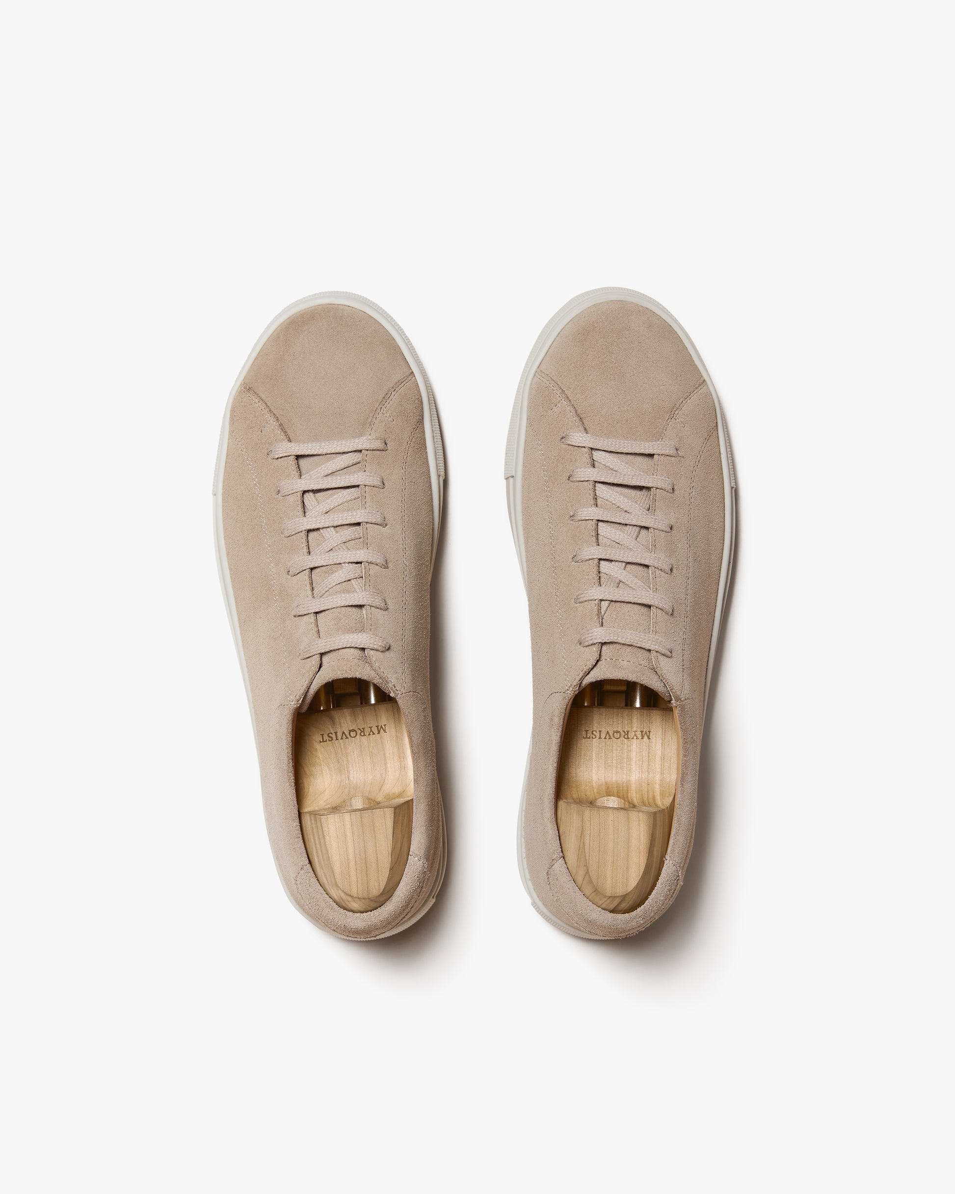 A top-down shot of the Oaxen II – Sand Suede sneakers with wooden shoe trees, against a clean white background.