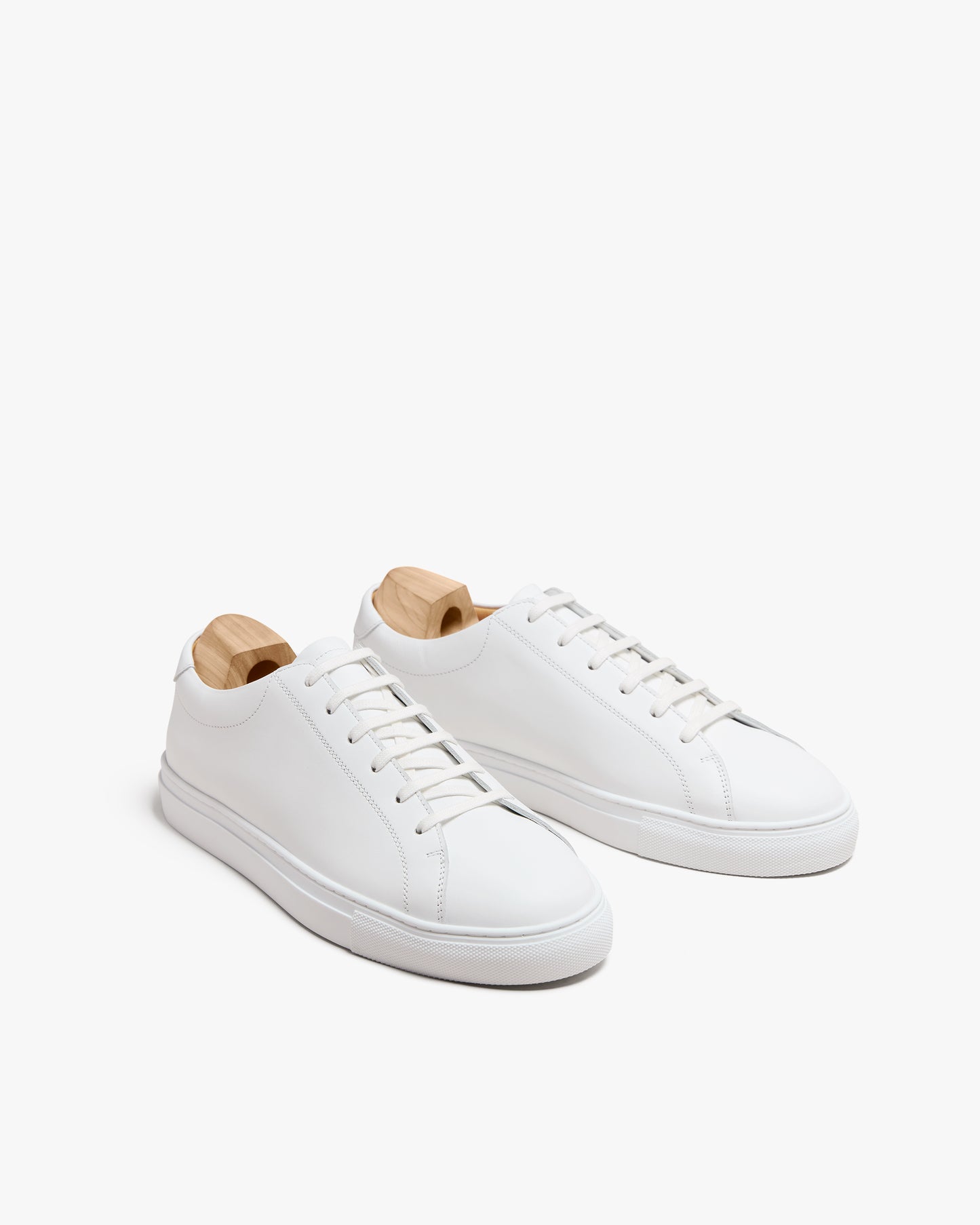 A pair of Oaxen II – White Calf sneakers with wooden shoe trees, displayed at an angle on a white background.