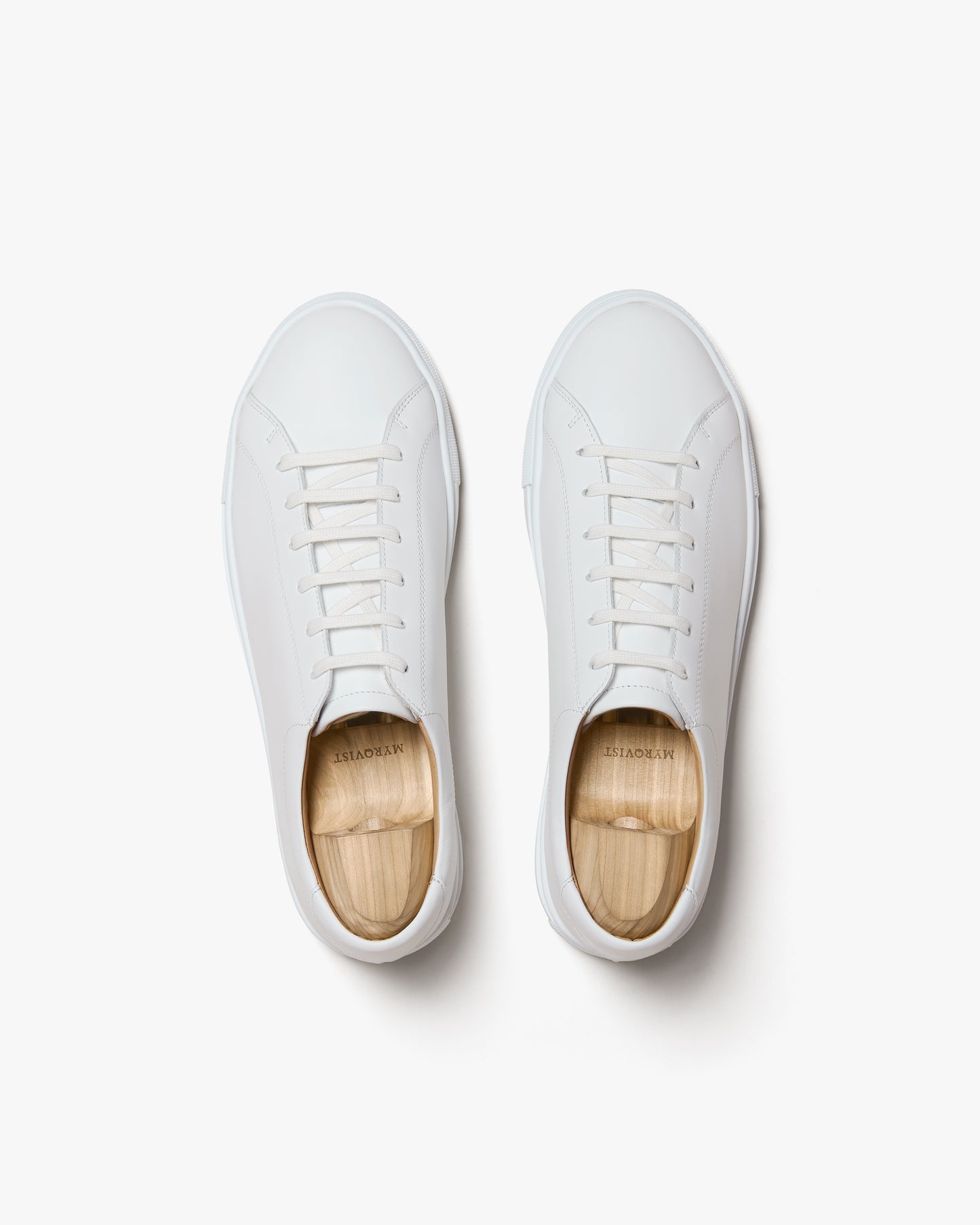 A top-down studio shot of the Oaxen II – White Calf sneakers, displayed with wooden shoe trees on a white background.