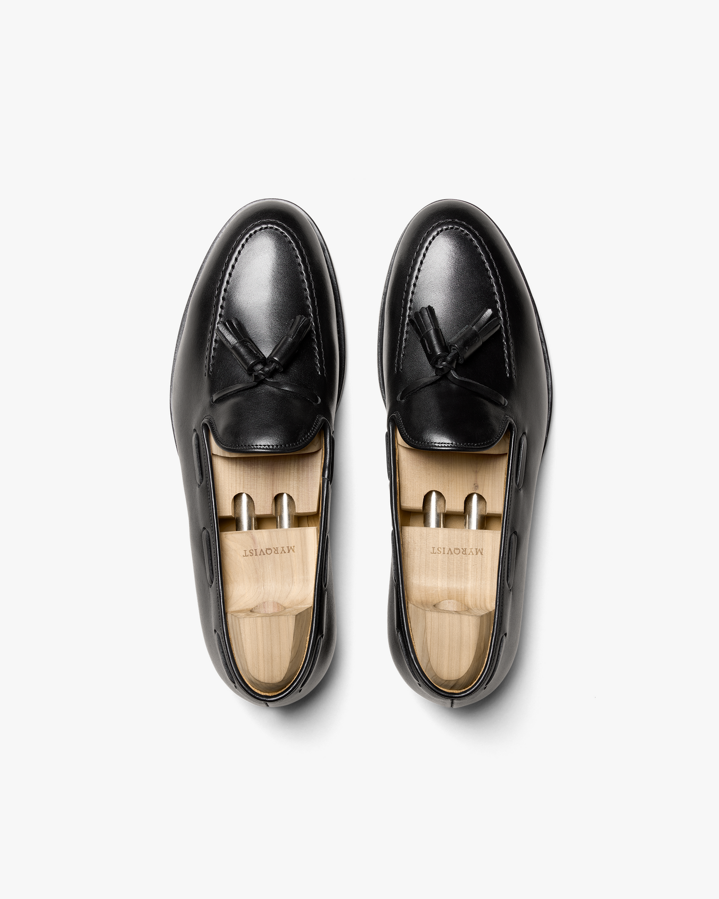 An overhead view of Mölle II – Black Calf tassel loafers, displayed with wooden shoe trees inside.