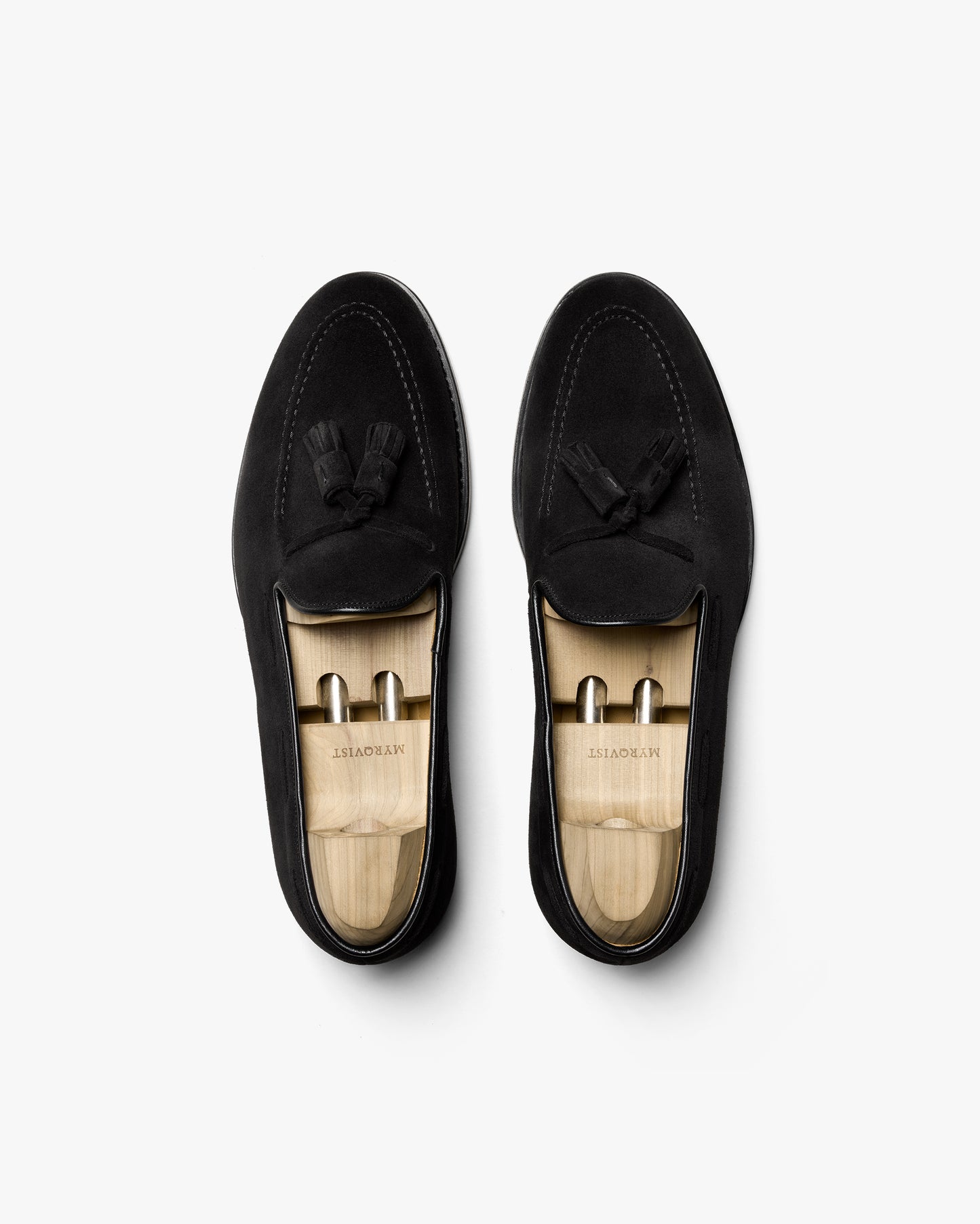 Overhead shot of a pair of Mölle II – Black Suede loafers with wooden shoe trees on a white background.