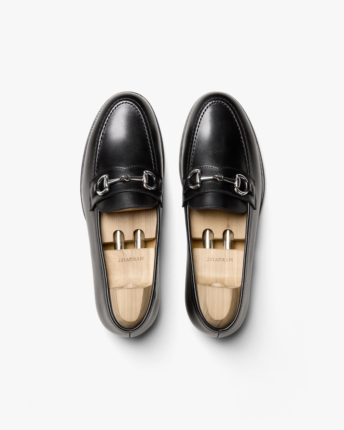 An overhead view of a pair of Karlberg – Black Calf horsebit loafers, styled with wooden shoe trees on a white background.
