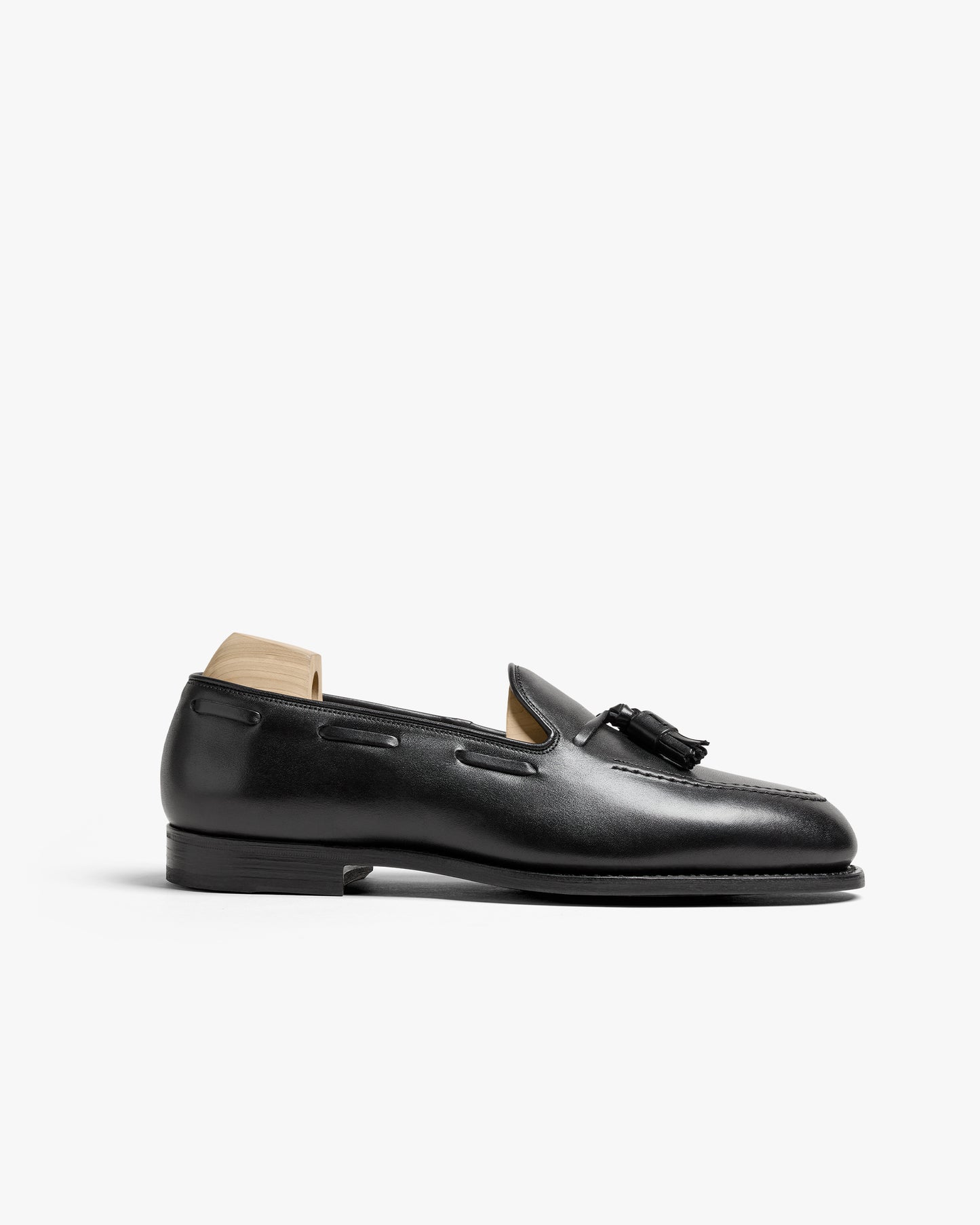 Profile view of the Mölle II – Black Calf loafer, showcasing its sleek design, tassel detailing, and leather sole.