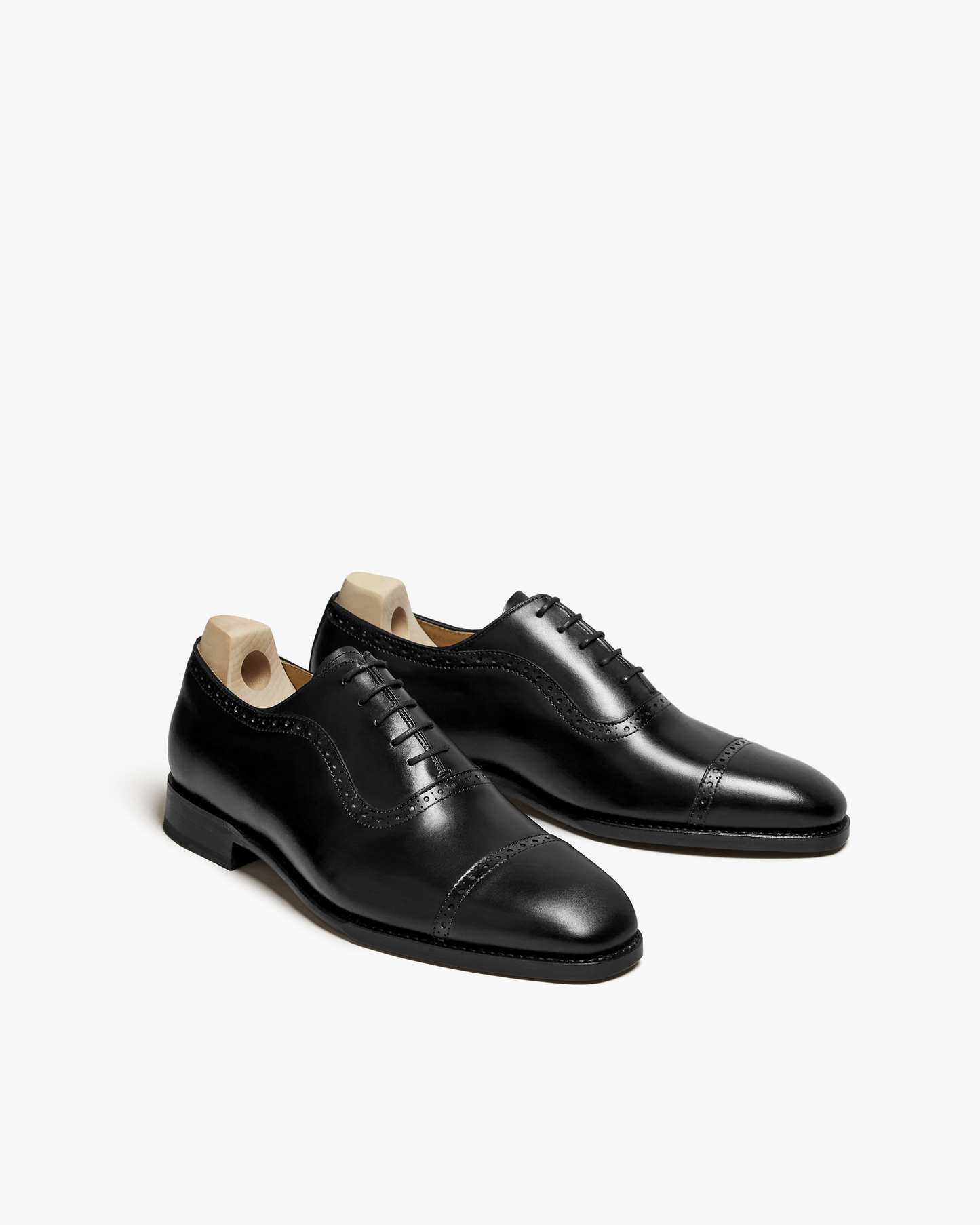 A pair of Skytteholm – Black Calf oxford shoes with brogue detailing, fitted with shoe trees against a white background.
