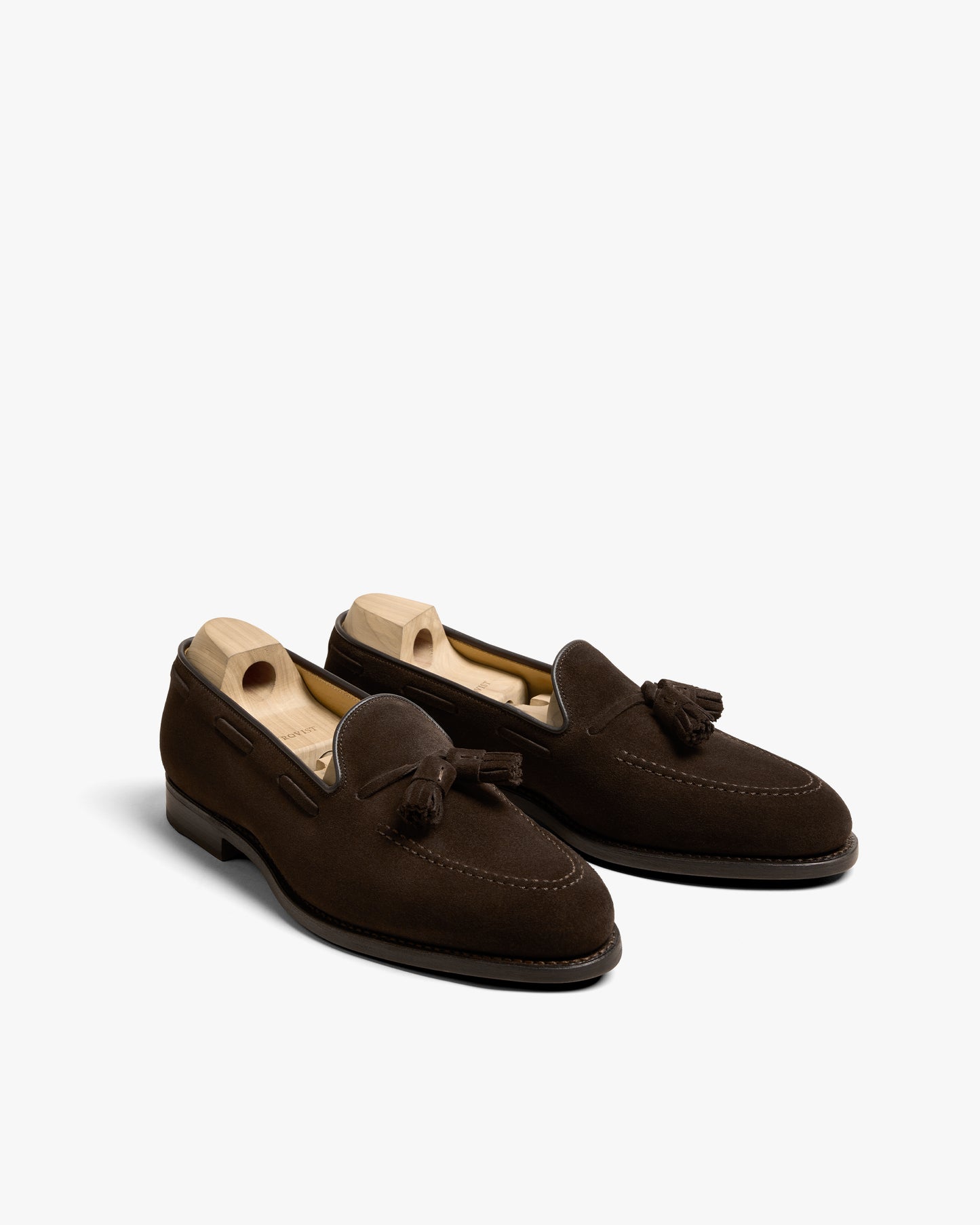 A pair of Mölle II – Dark Brown Suede tassel loafers with wooden shoe trees inside, shot against a white background.