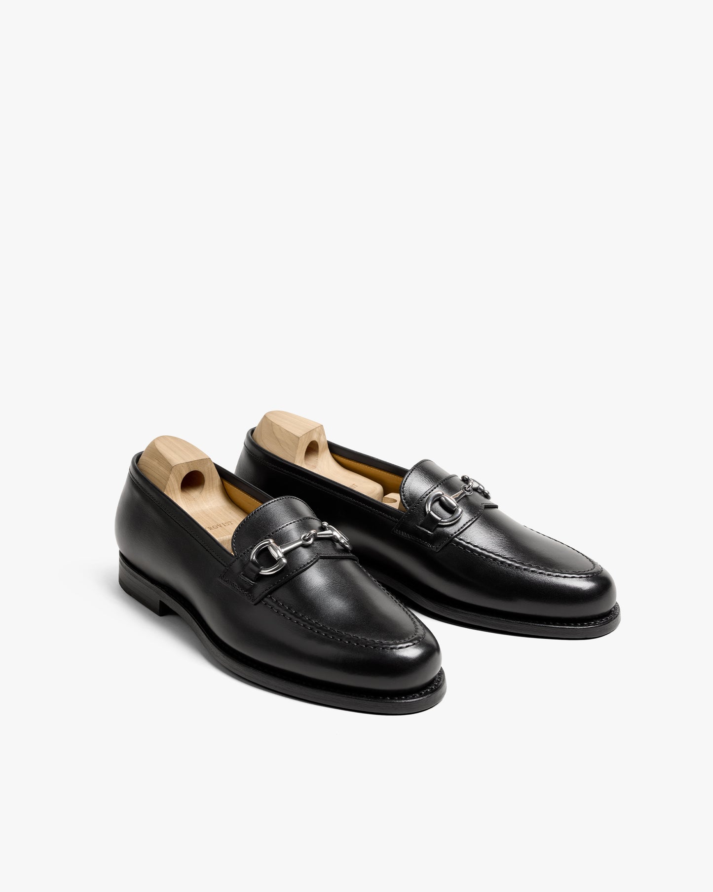 A pair of Karlberg – Black Calf horsebit loafers with wooden shoe trees, angled on a white studio background.