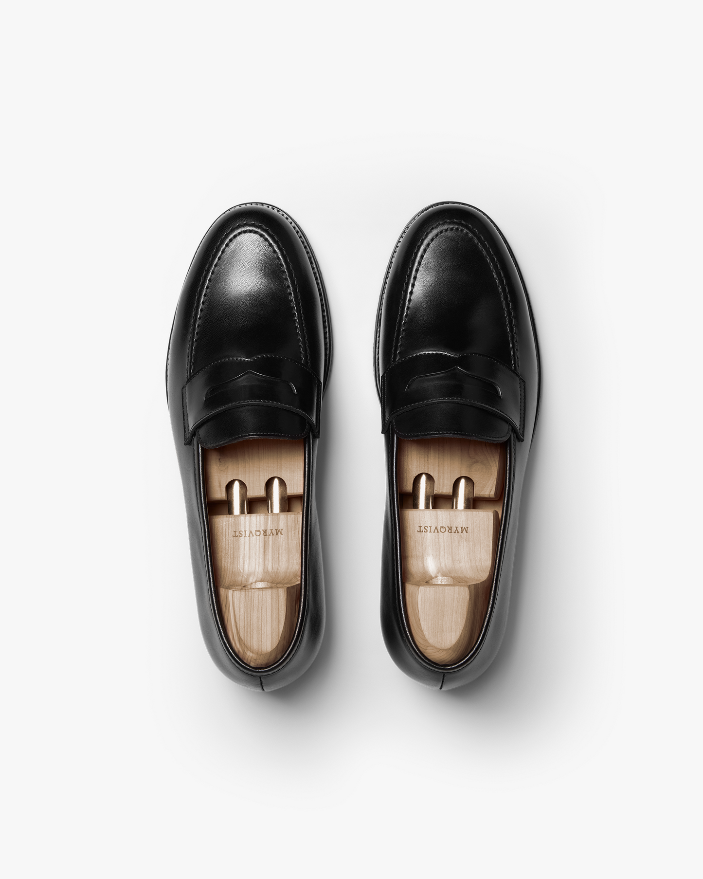 Overhead view of a pair of Stenhammar II – Black Calf penny loafers fitted with wooden shoe trees on a white background.